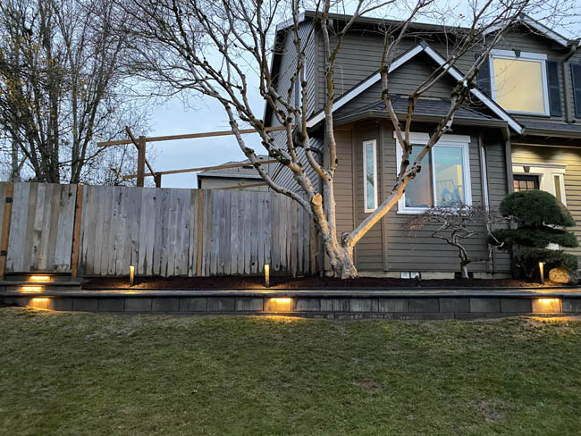 Front yard retaining wall with integrated path lighting at dusk