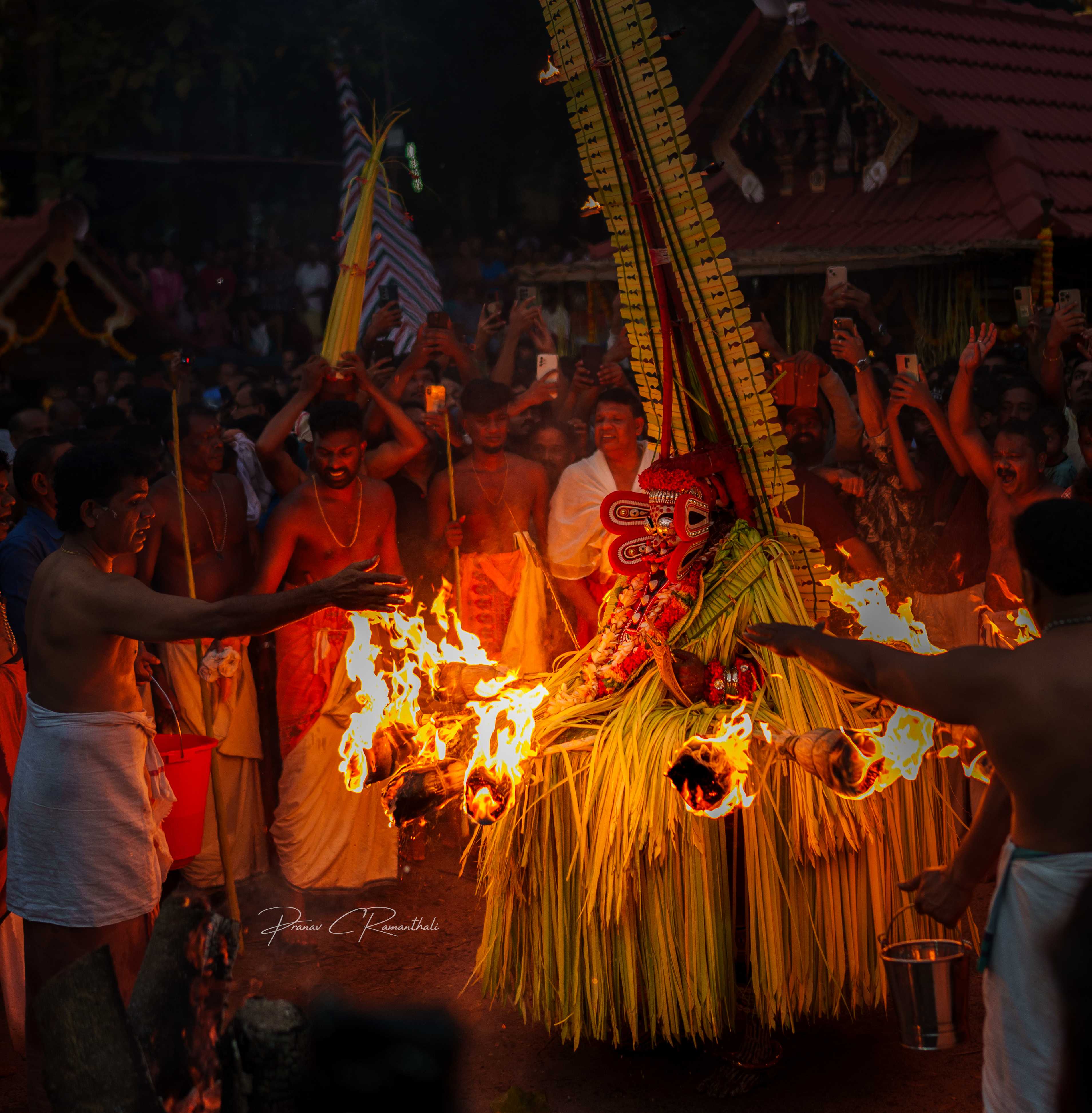 Theyyam performer surrounded by fire torches and enthusiastic devotees