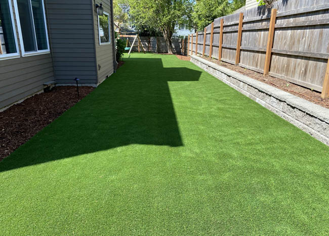 Backyard synthetic turf installation alongside cedar fence