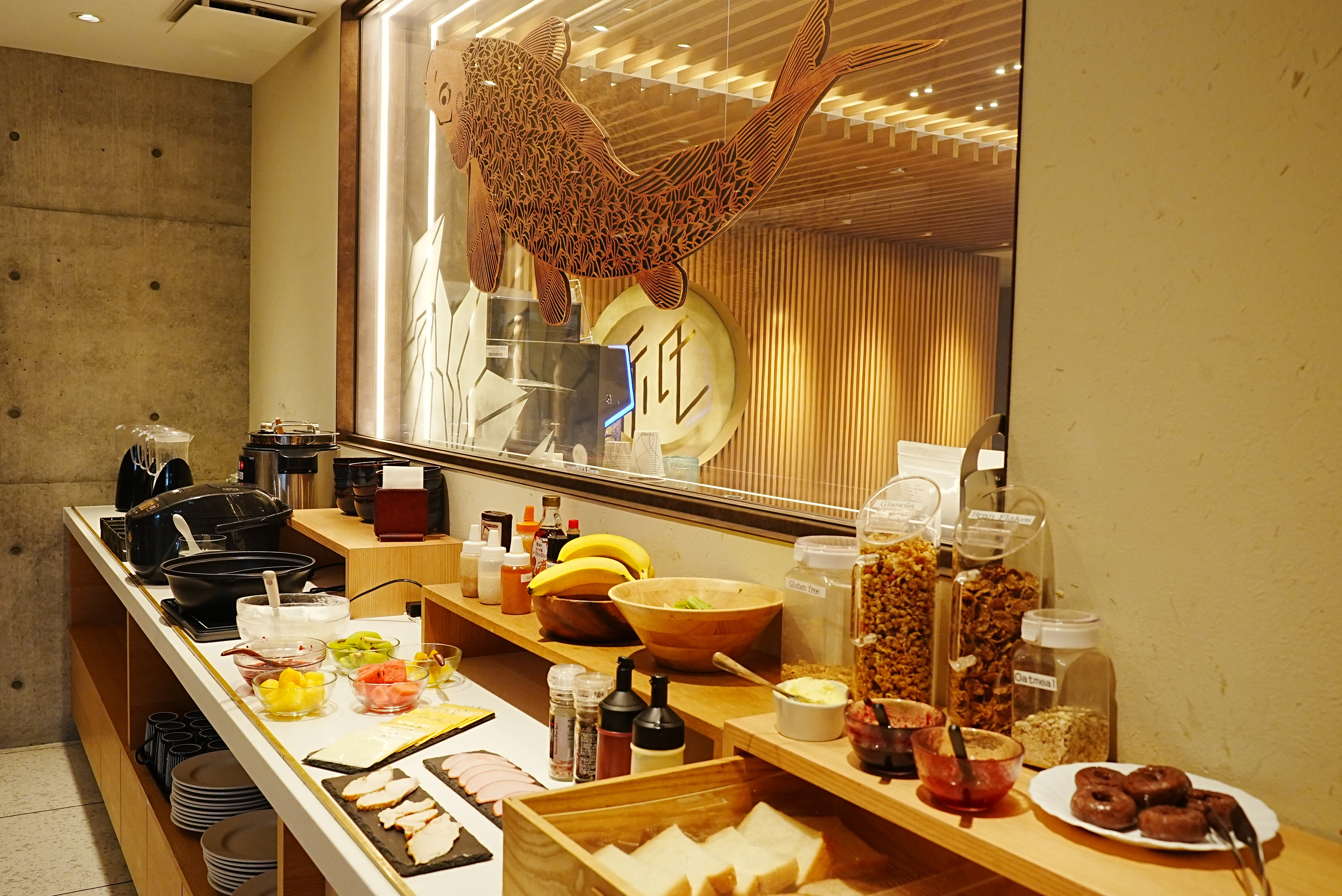 Breakfast buffet counter with fresh bread, seasonal fruit, granola, and carved koi wood art