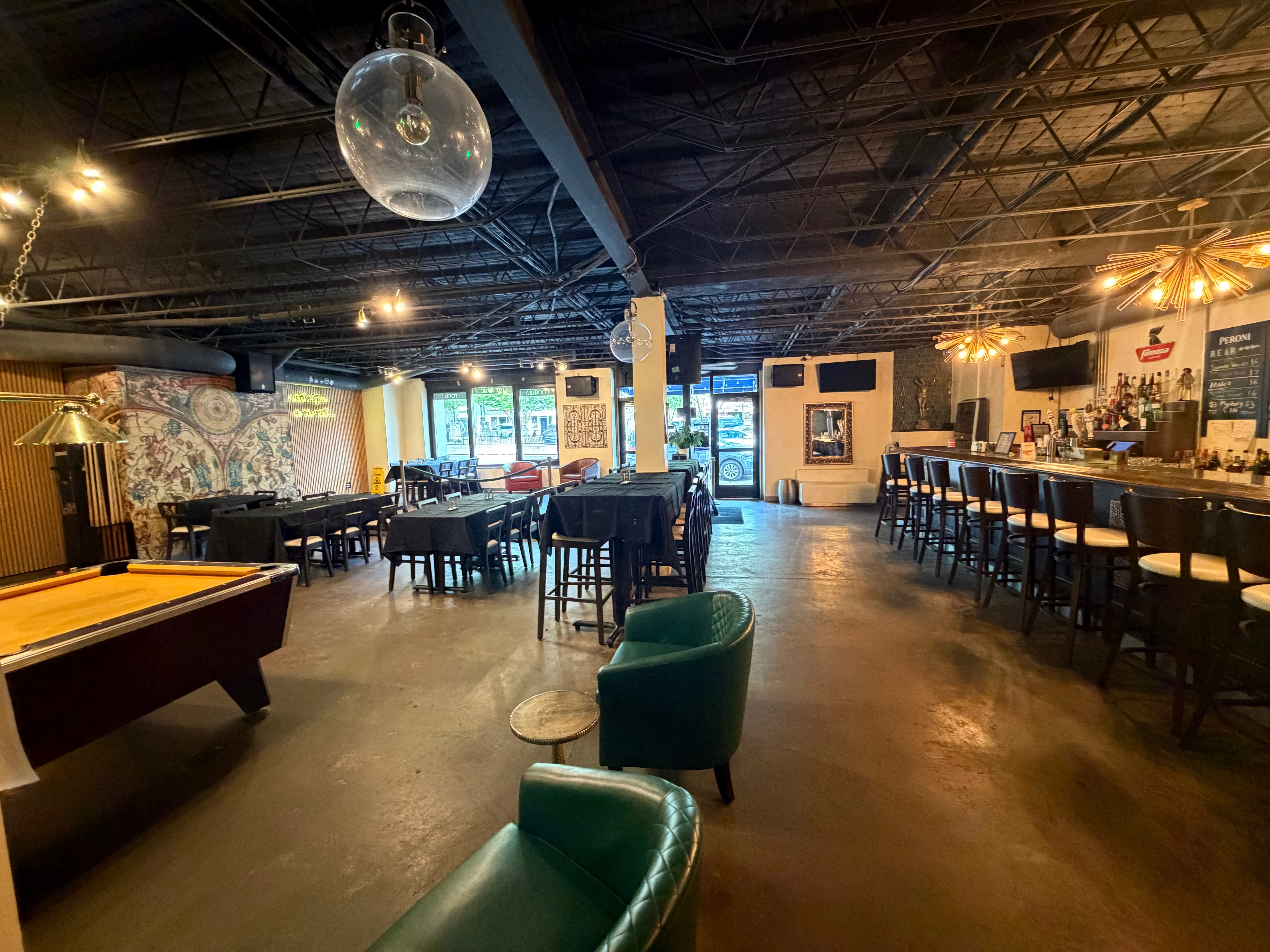 Wide-angle view of the main bar area with pool table, bar counter, and lounge chairs
