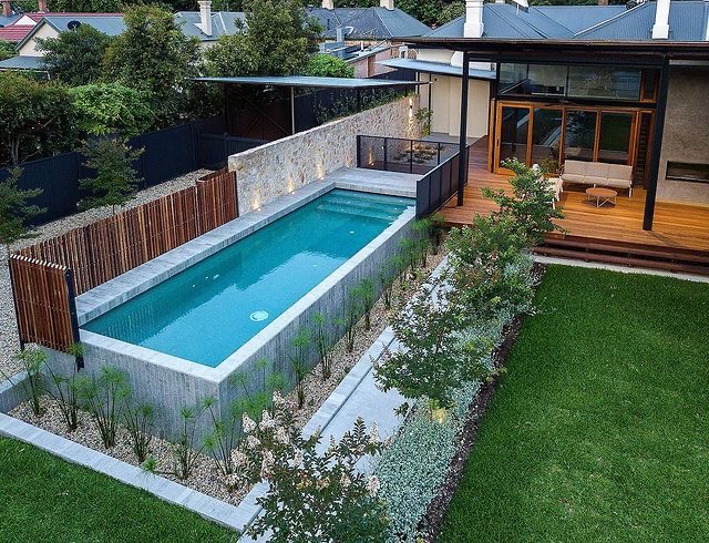 Modern container pool with concrete sides and wooden deck in a green backyard