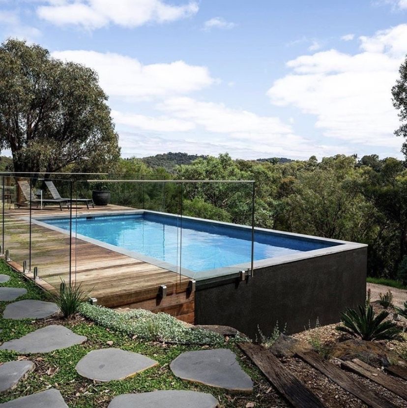 Container pool with glass railing and wooden deck overlooking scenic hills