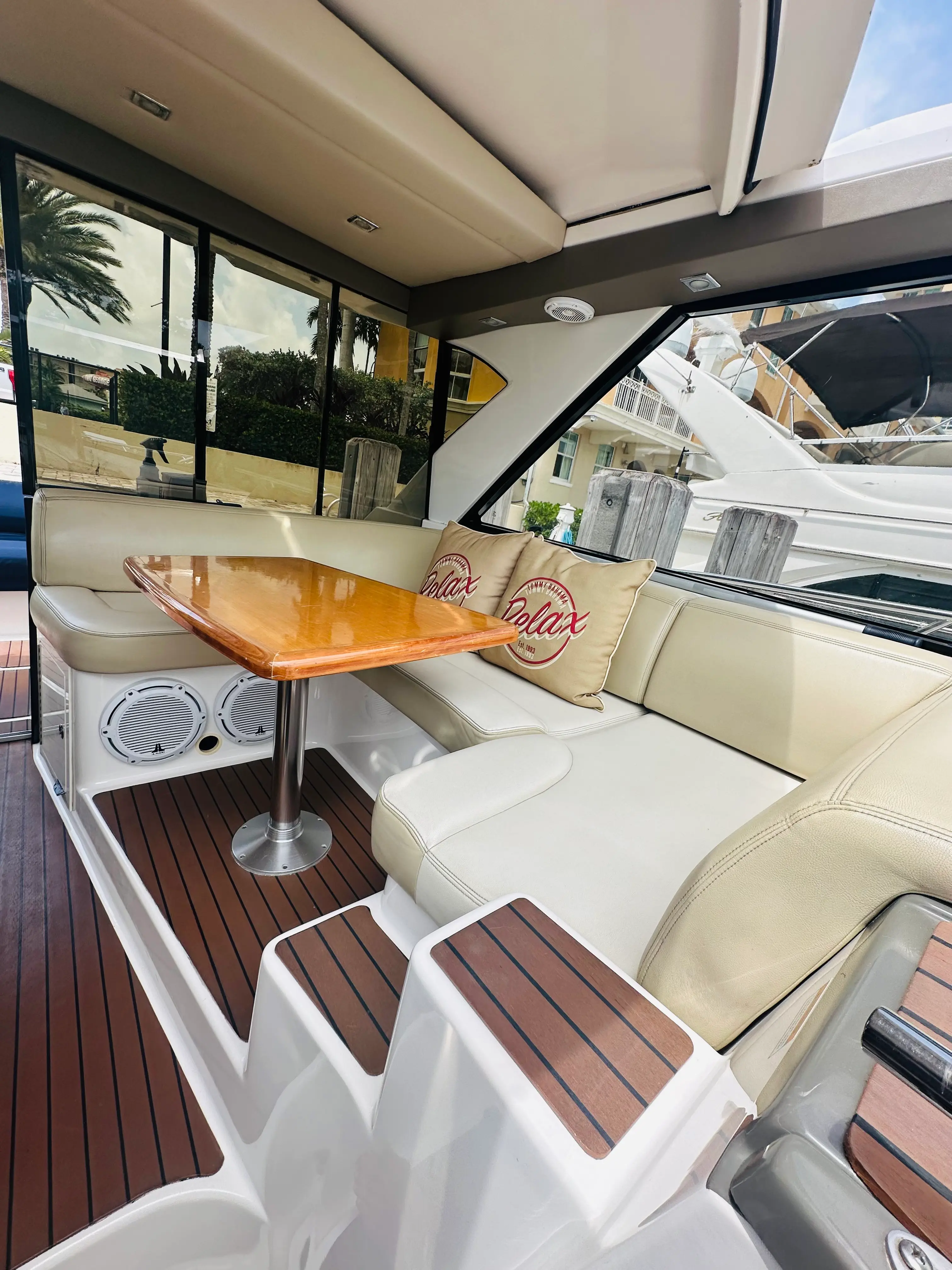 Air-conditioned indoor dining saloon aboard the Elite Sport Yachts Regal Sport Coupe, featuring cream leather L-shaped seating, a teak pedestal dining table, and JL Audio speakers