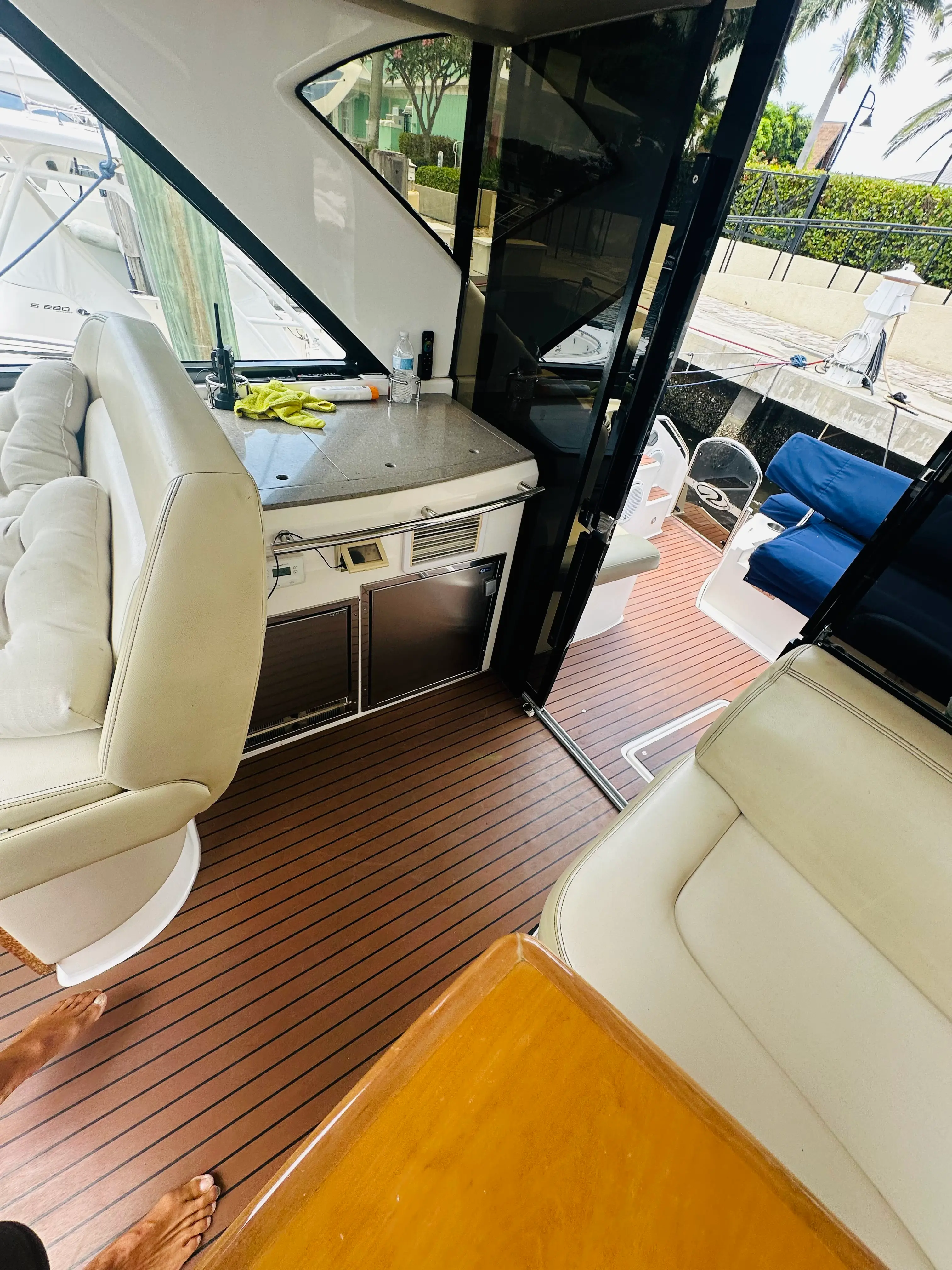 Interior lounge saloon of the Elite Sport Yachts Regal Sport Coupe showing cream leather seating, built-in refrigerator, teak flooring, and an open glass door leading to the cockpit