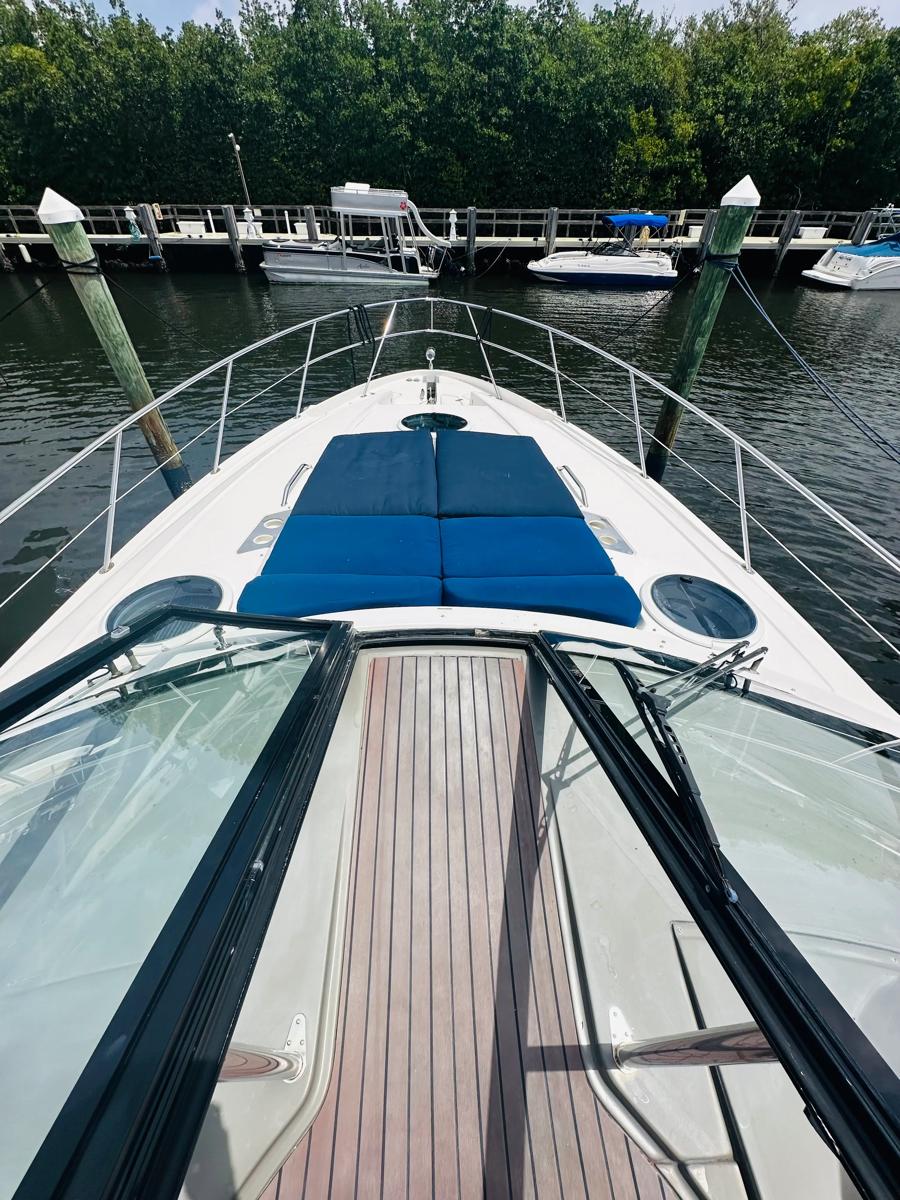 Forward view from the helm of the Elite Sport Yachts Regal Sport Coupe along the teak walkway toward the bow sunpad area, with glass windshield panels and marina dock visible