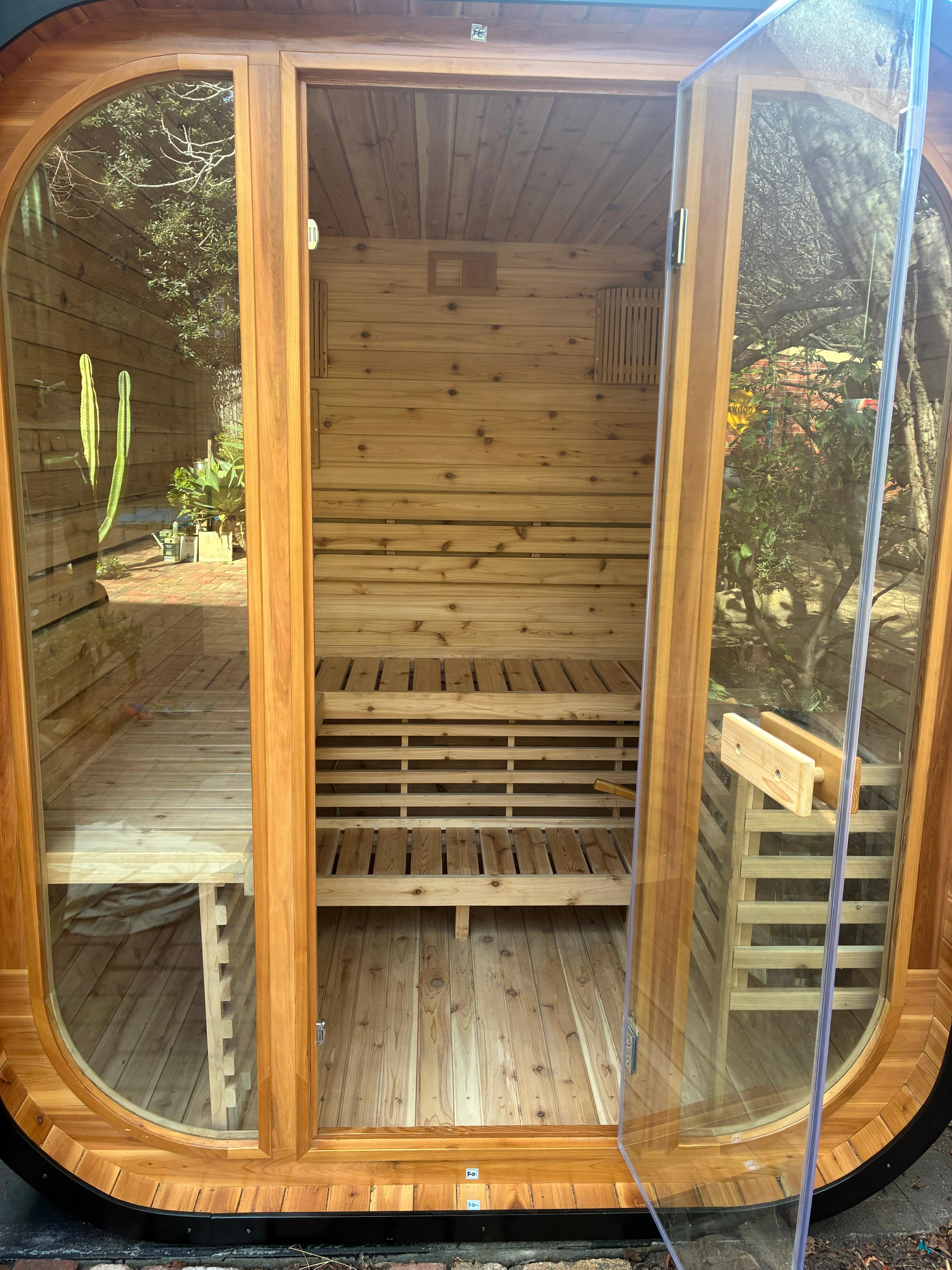 Completed Canadian Red Cedar sauna installed in a Melbourne backyard, viewed front-on through the full-height glass door with the tiered cedar bench seating visible inside