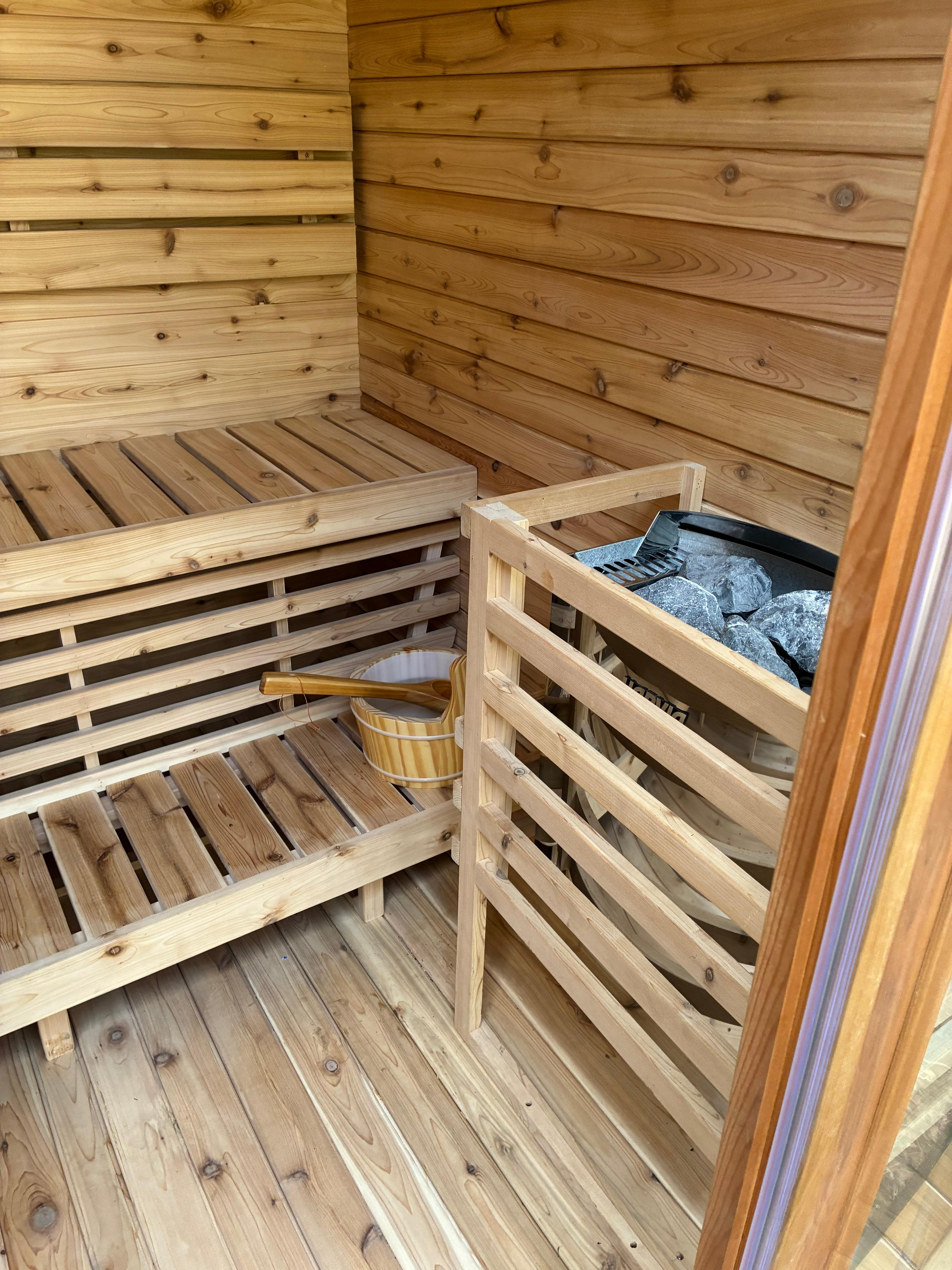 Finished cedar interior with the Harvia heater and timber guard, bench seating and a traditional bucket and ladle