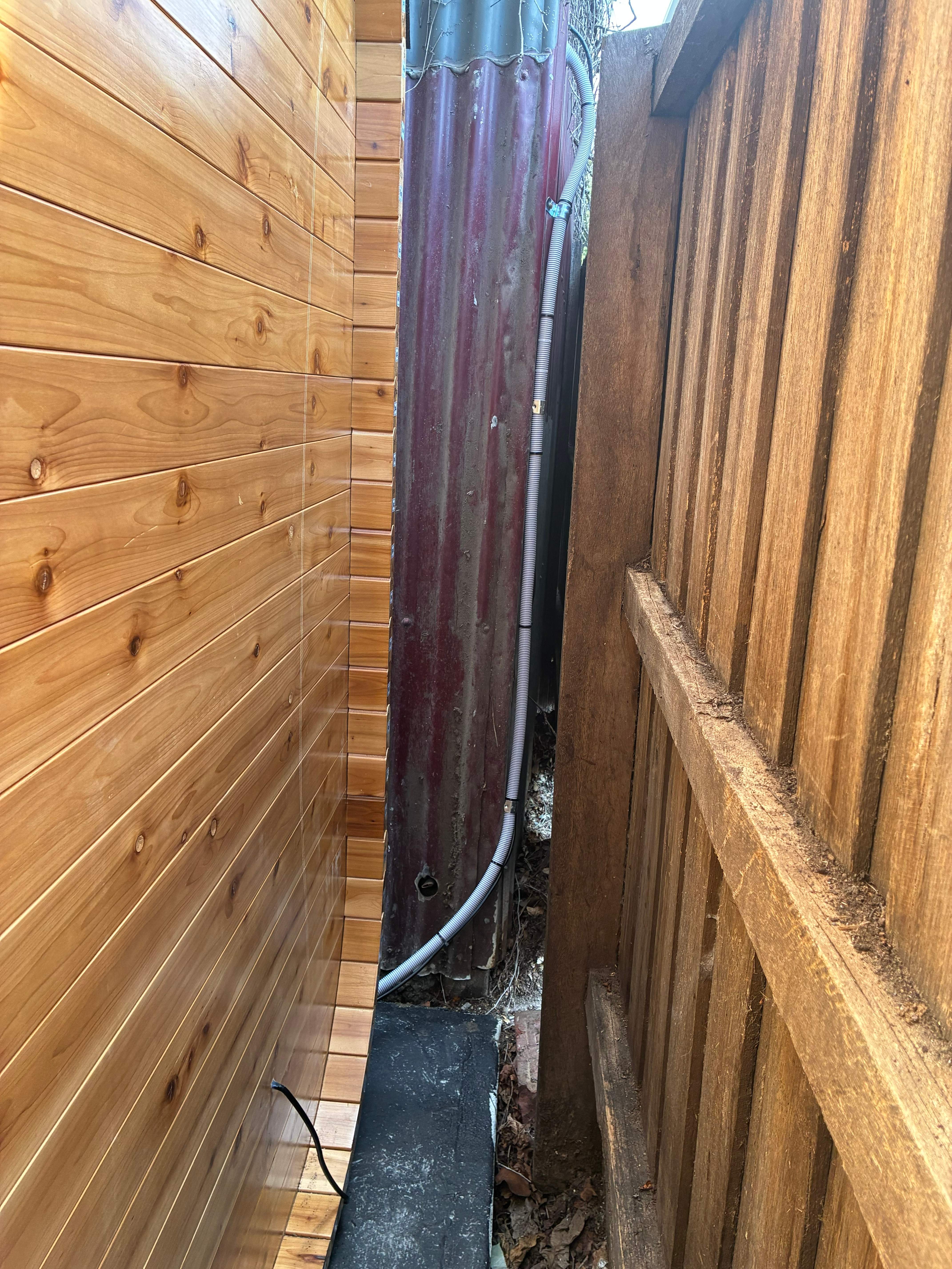 Power conduit routed neatly between the finished sauna and the boundary fence
