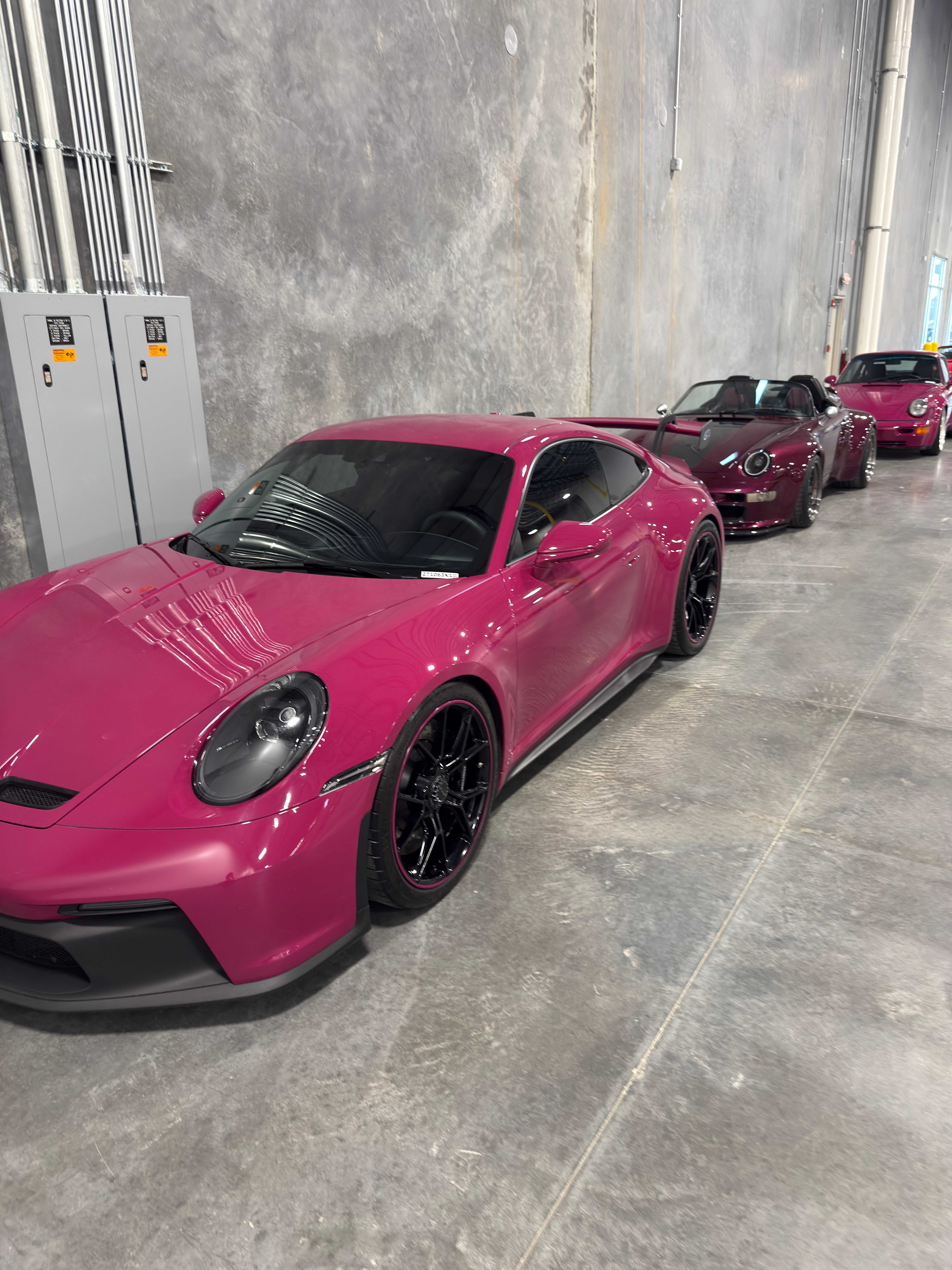 Porsche 992 S/T in Ruby Star magenta alongside a dark Targa and another 911