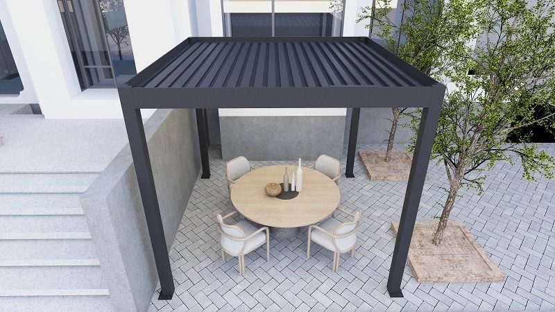 Overhead view of a dark charcoal aluminum pergola with closed louvered slats over a round dining table on a cobblestone courtyard