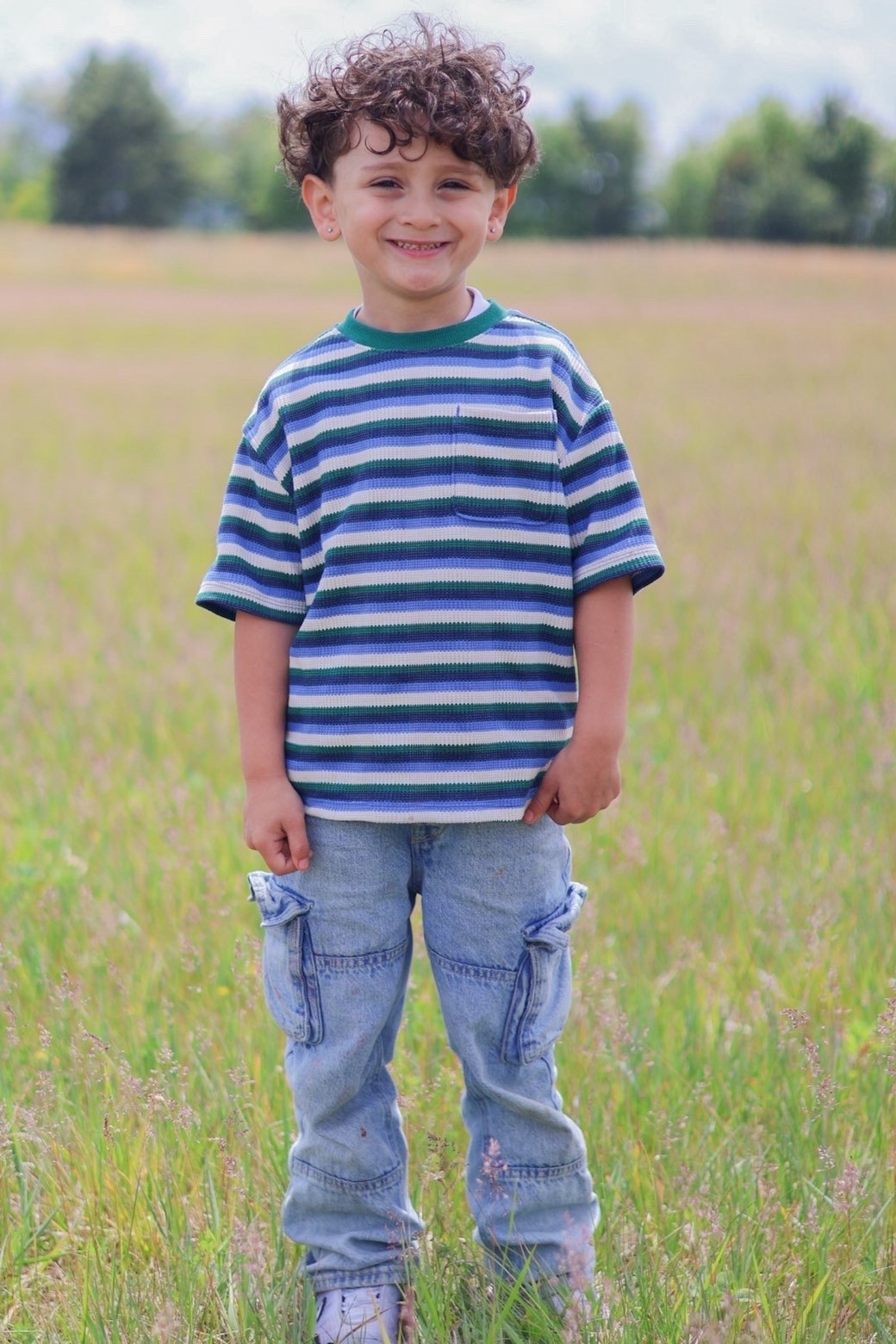 Young boy with curly hair smiling in a meadow