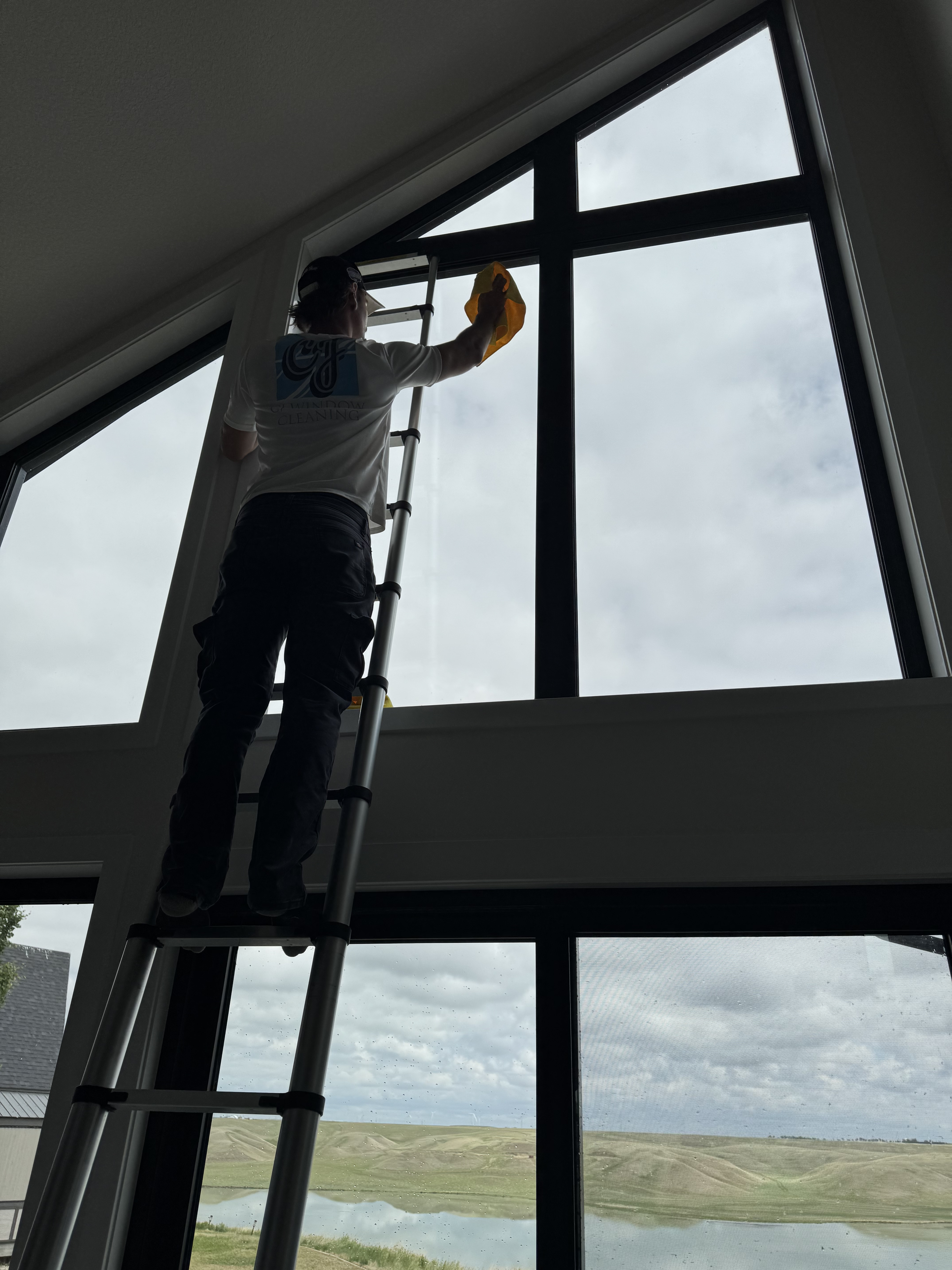 CJ Windows technician on a ladder cleaning tall peaked interior windows