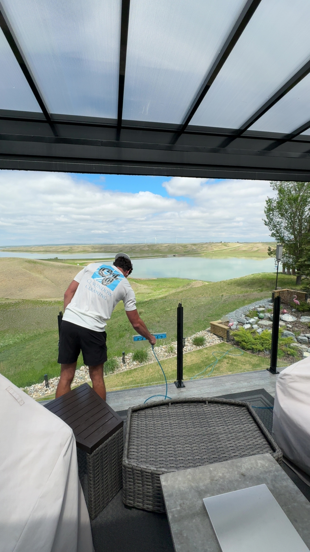 CJ Windows technician cleaning glass railing on a lakeside patio