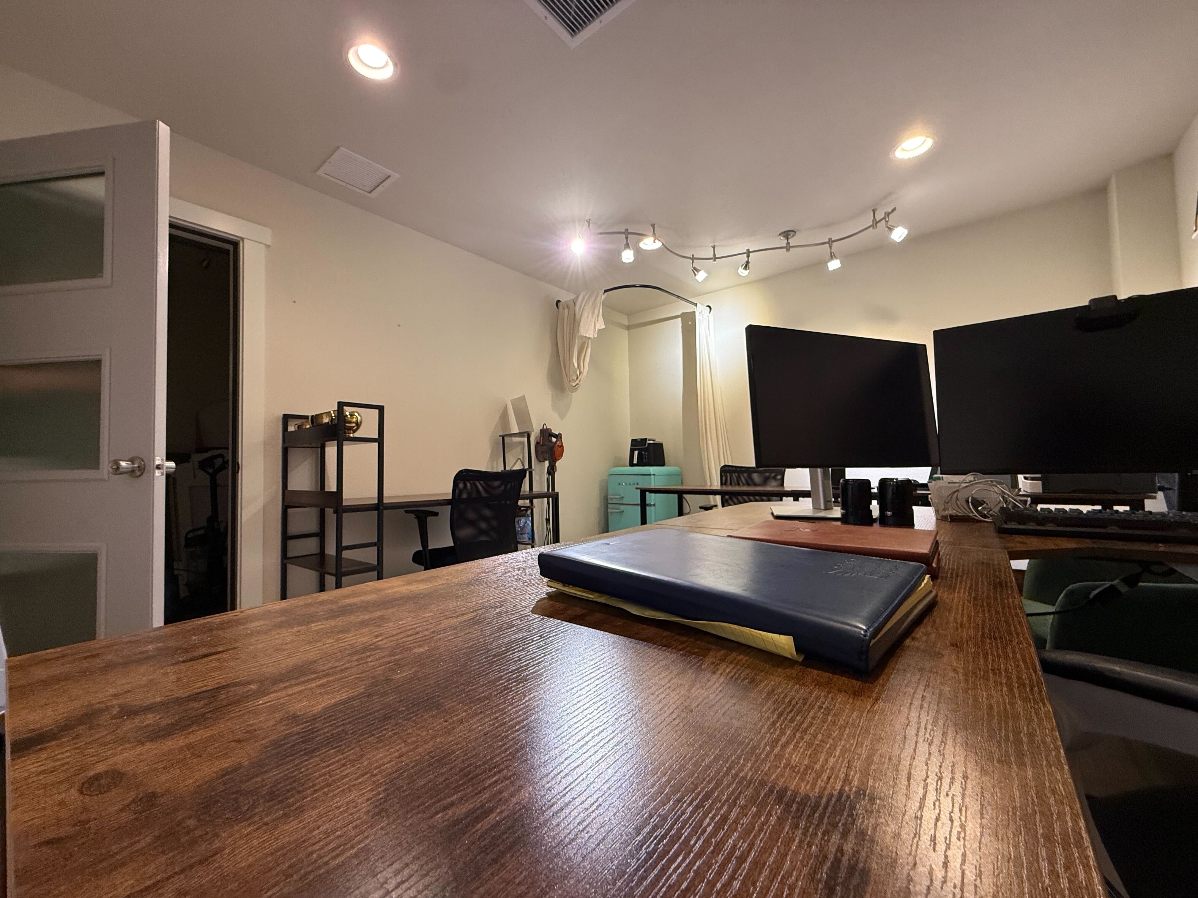 Rustic wooden desk with notebooks, dual monitors and track lighting