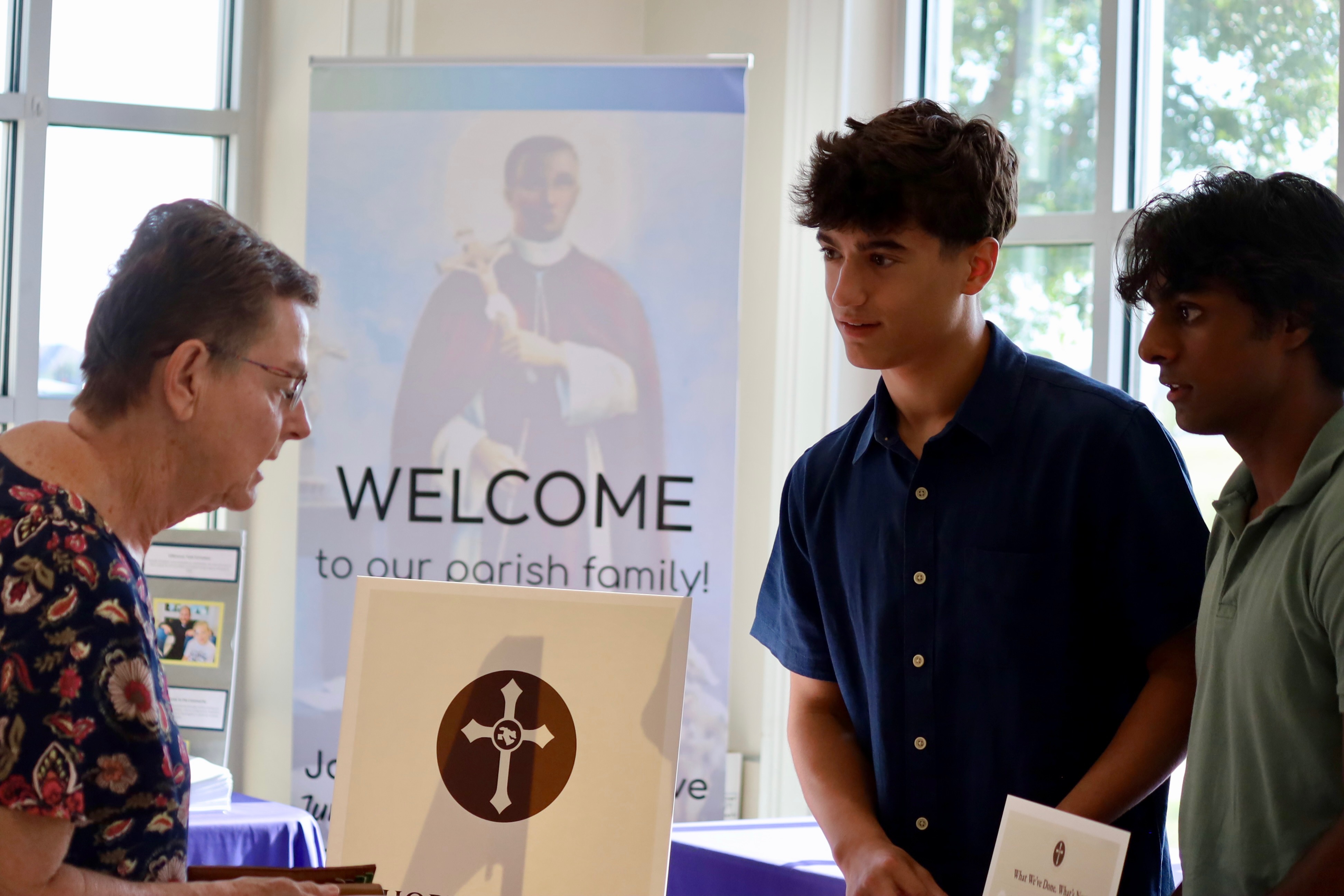 A founder speaking with a parishioner in front of a parish welcome banner