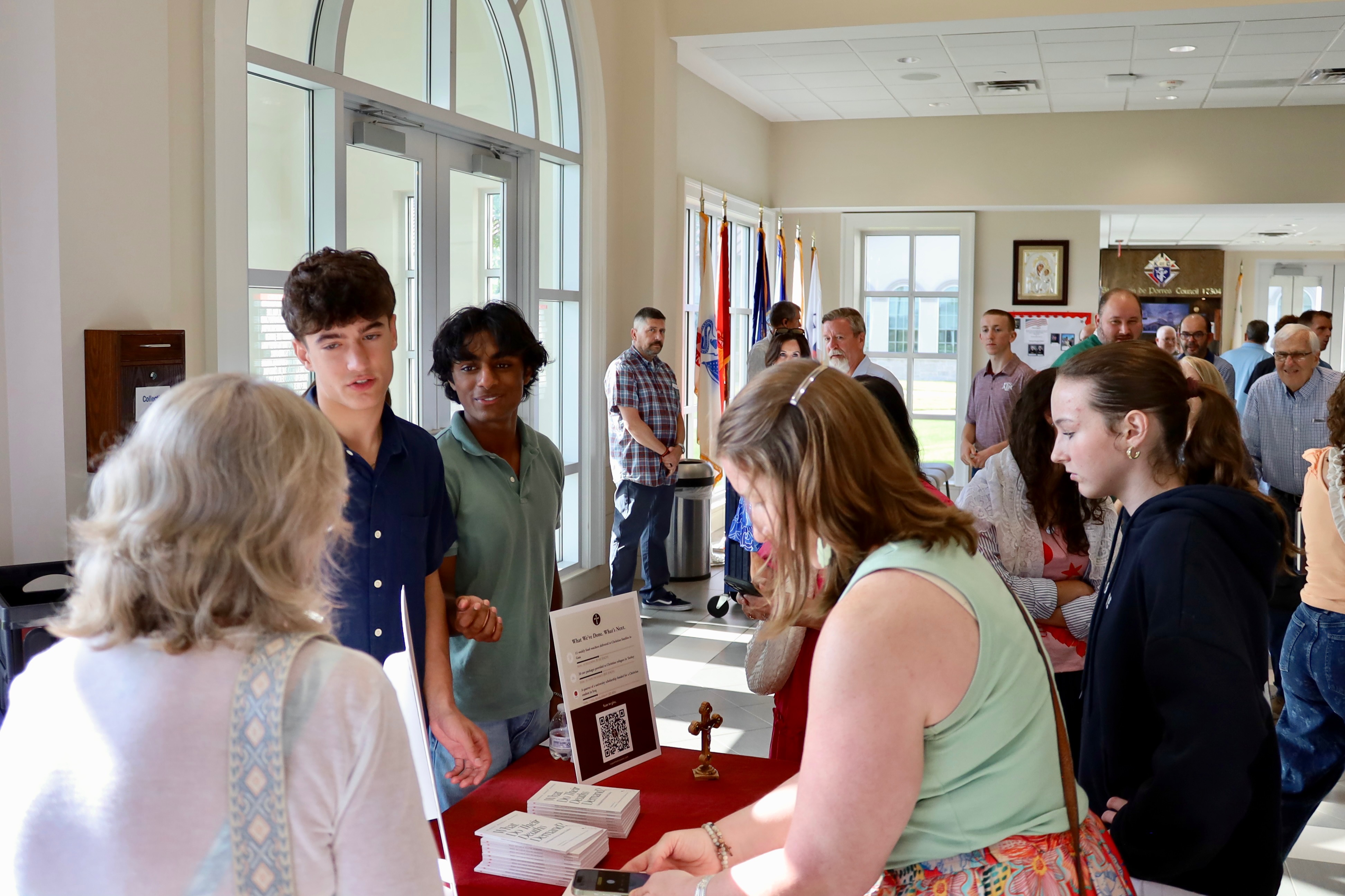 The founders talking with attendees at the outreach table with a donation QR code and books