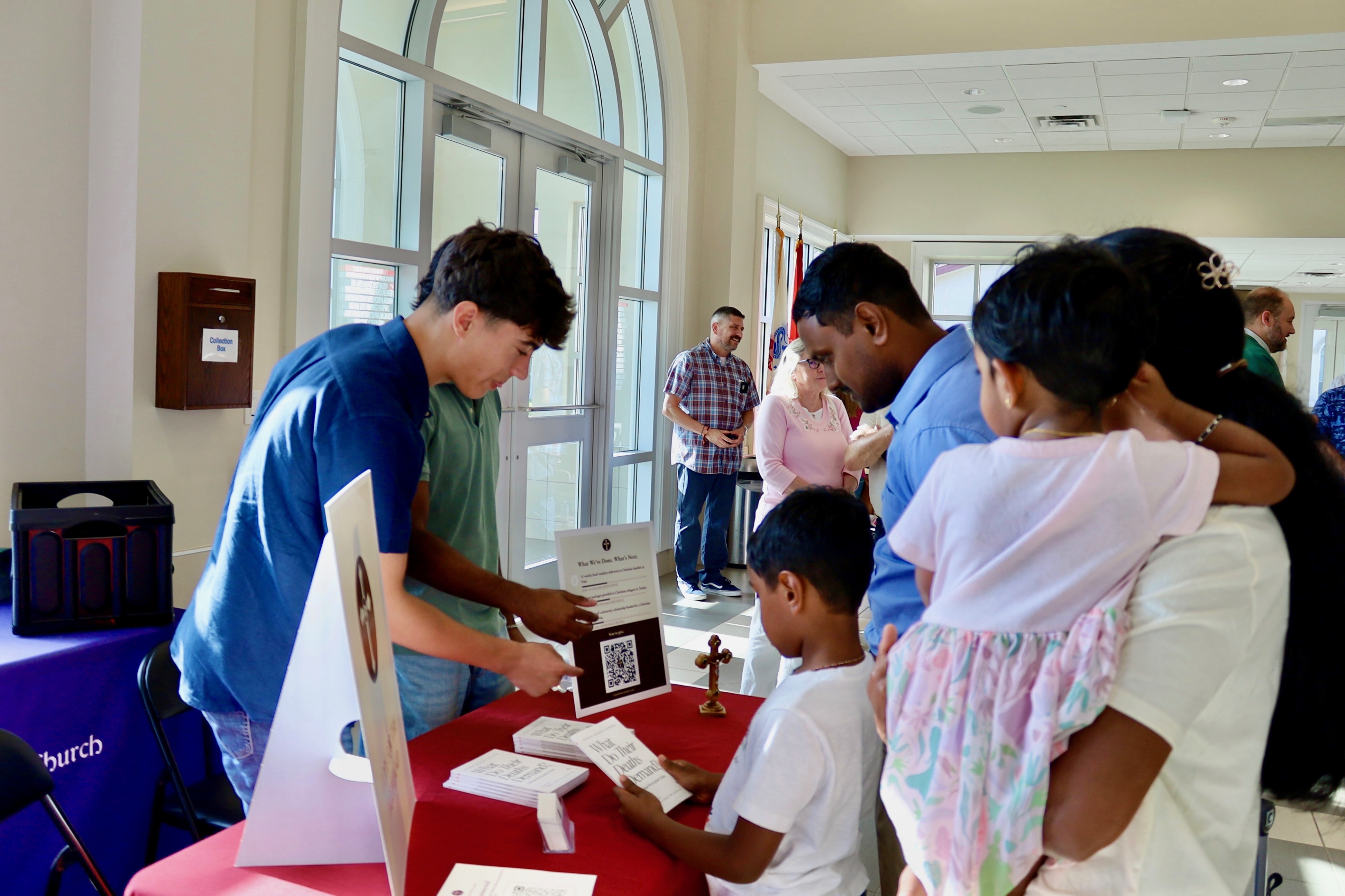 A founder showing the donation QR code to a family with young children at the outreach table