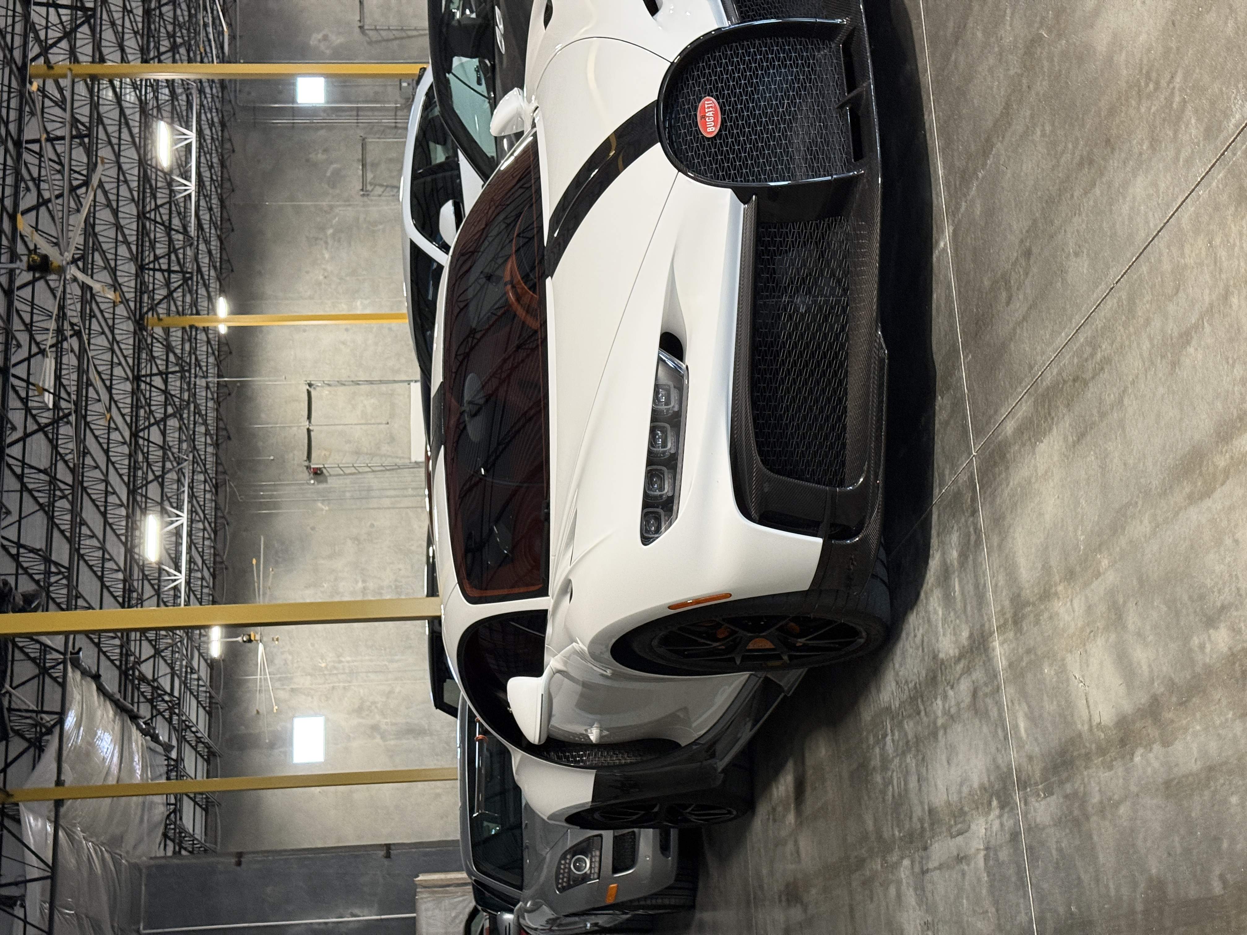 Bugatti Chiron Pur Sport white with black carbon stripe, 3/4 front in warehouse, SLS behind