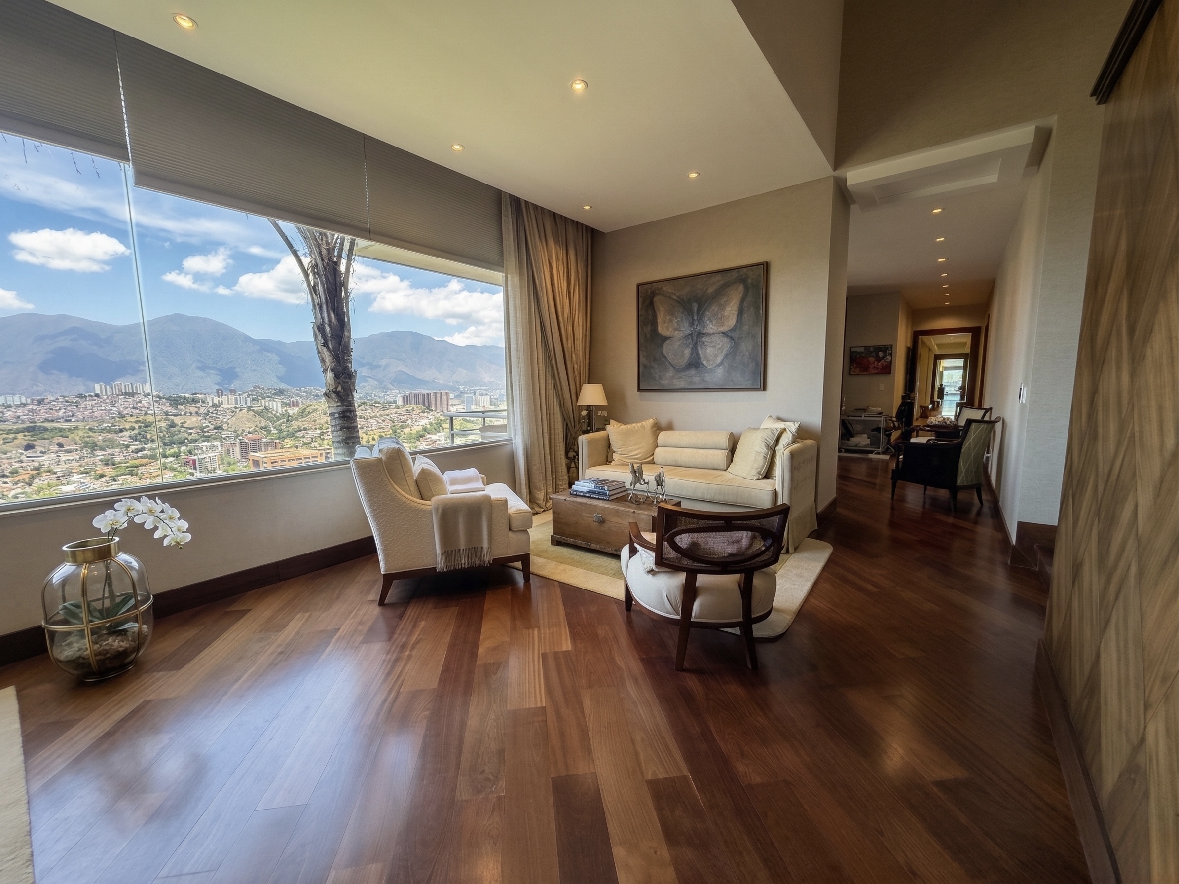 Elegant living room with panoramic windows showcasing the Avila mountains, hardwood floors and refined furnishings, La Trinidad estate Caracas