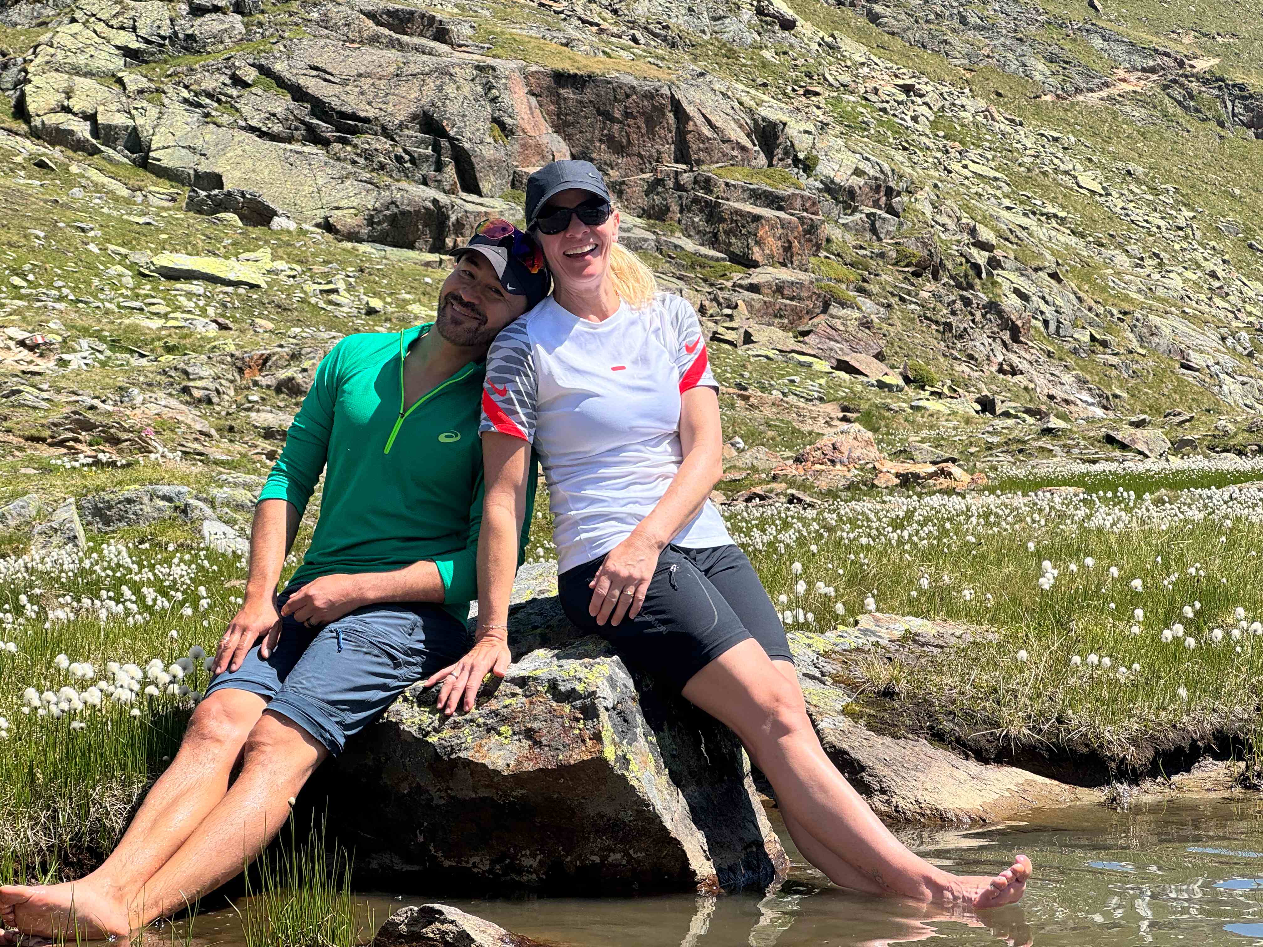 Zwei Teilnehmer rasten lachend an einem Bergsee mit Wollgras