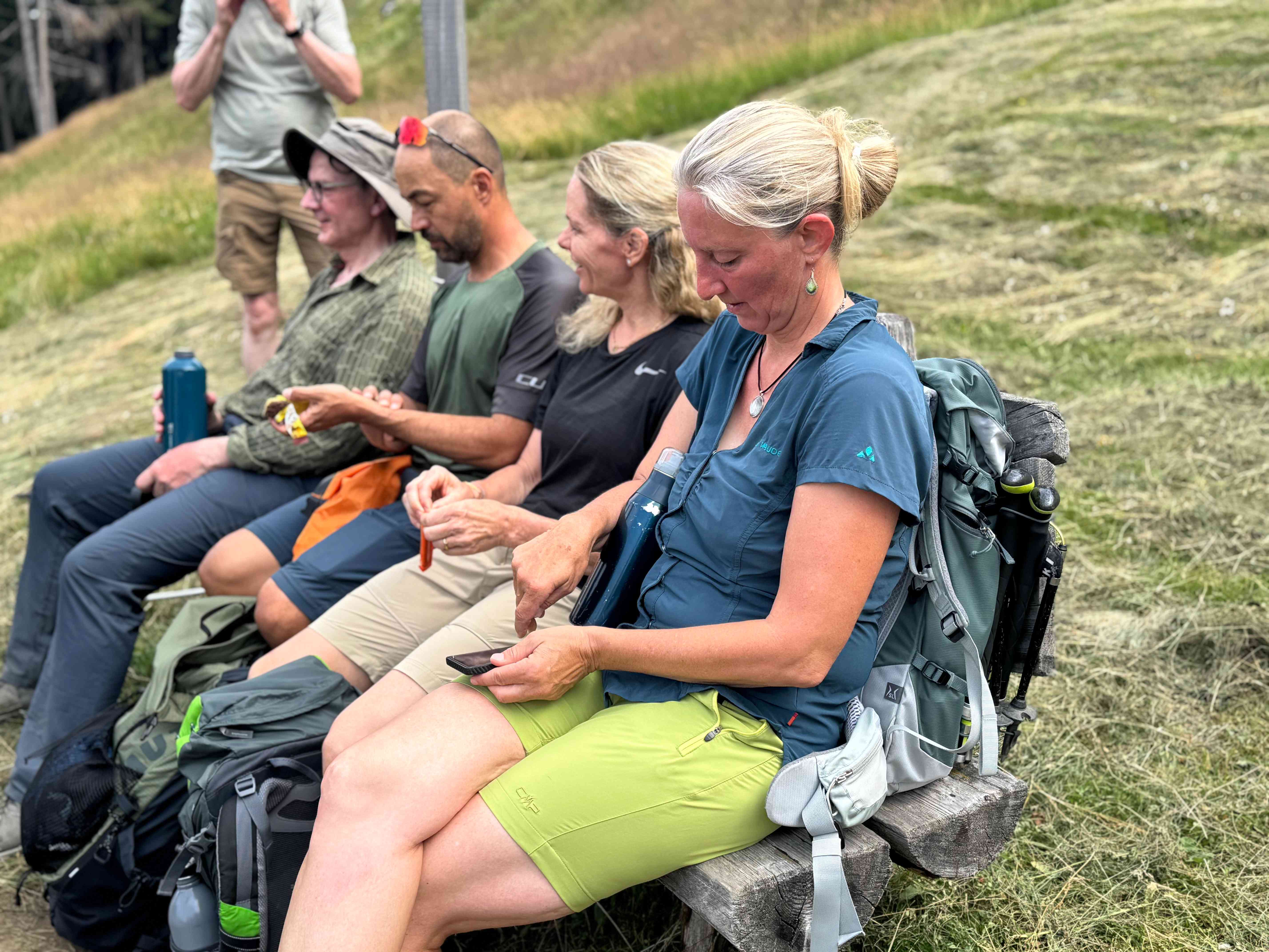 Teilnehmer machen Pause auf einer Holzbank in den Bergen