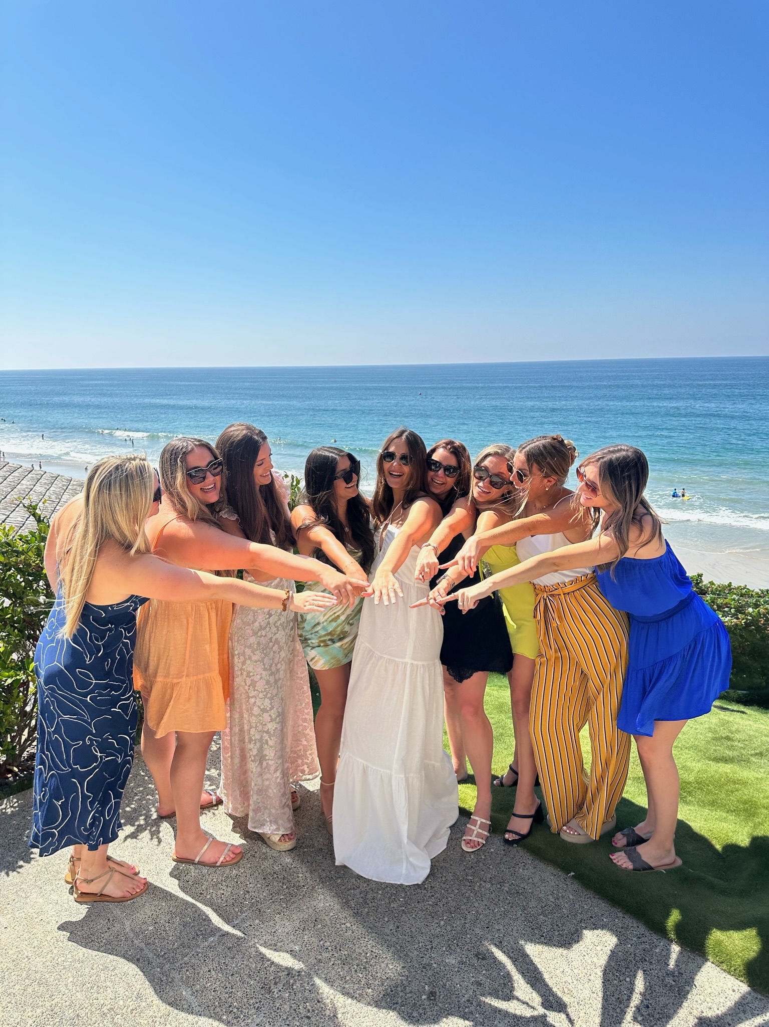 Large group of women celebrating on coastal cliff with ocean backdrop - bridal party celebration
