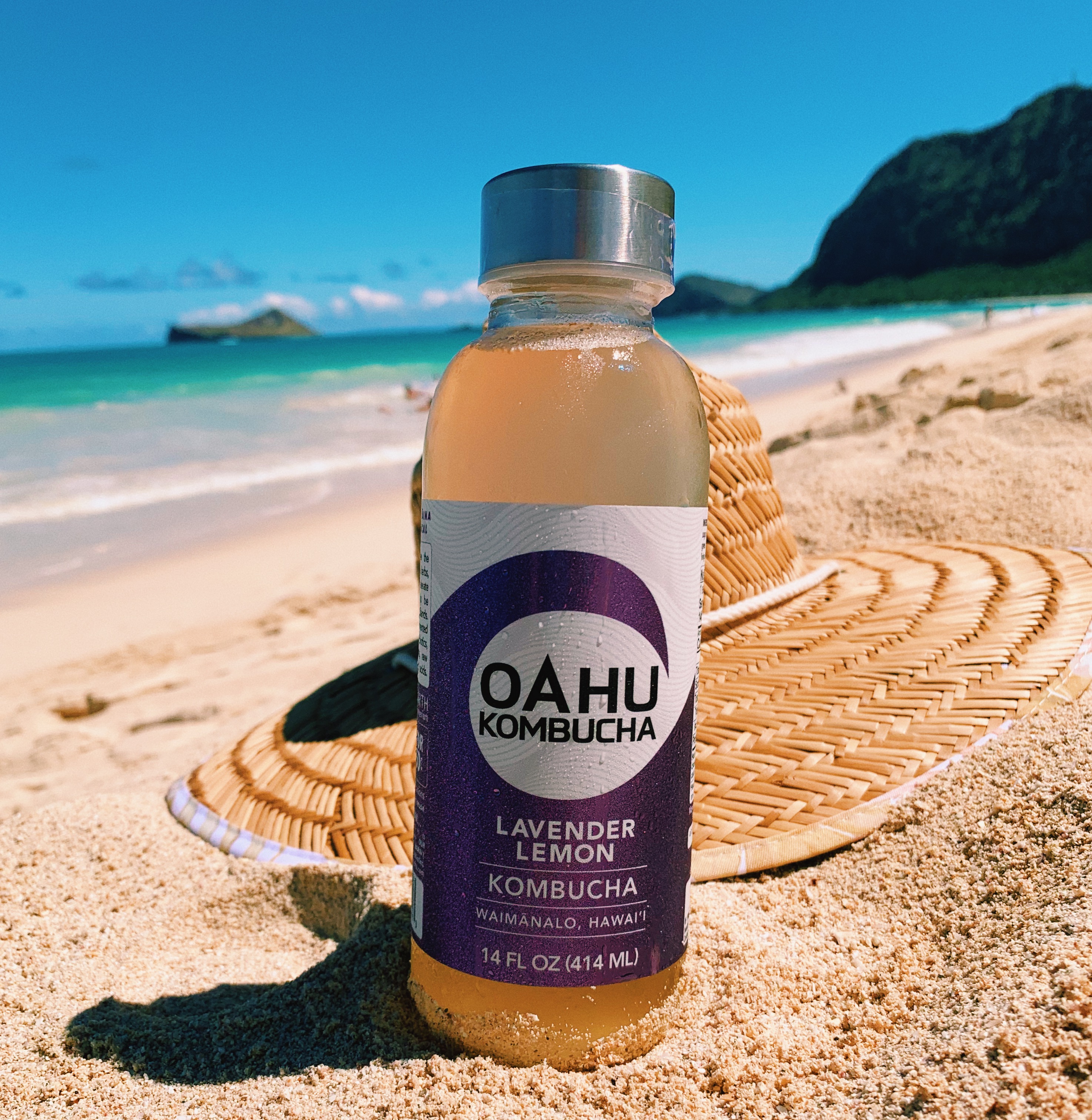 Lavender Lemon bottle beside a woven hat on the beach