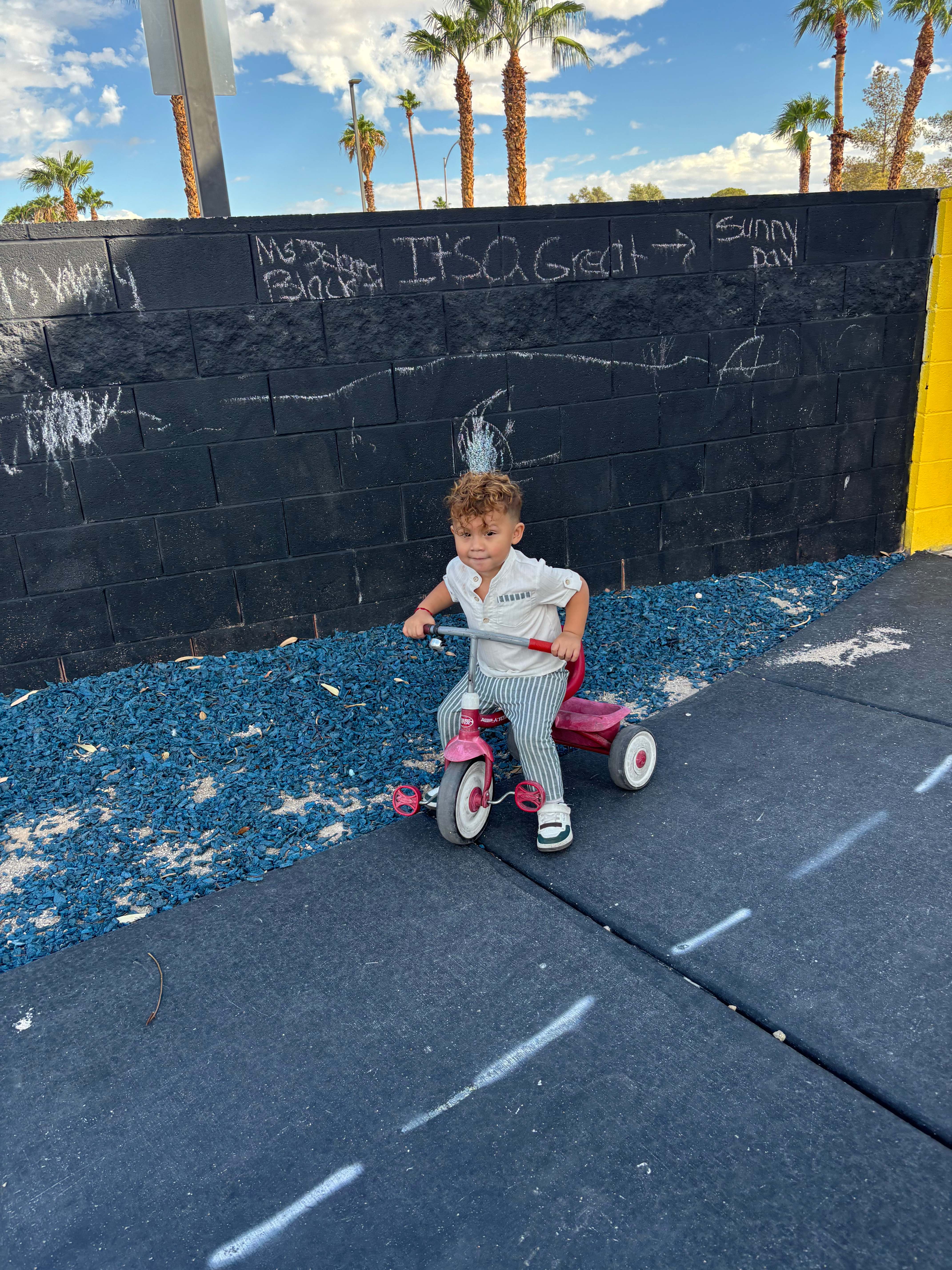 Sunny Day Foundation outdoor play activity with child riding a tricycle alongside the Sunny Day wall