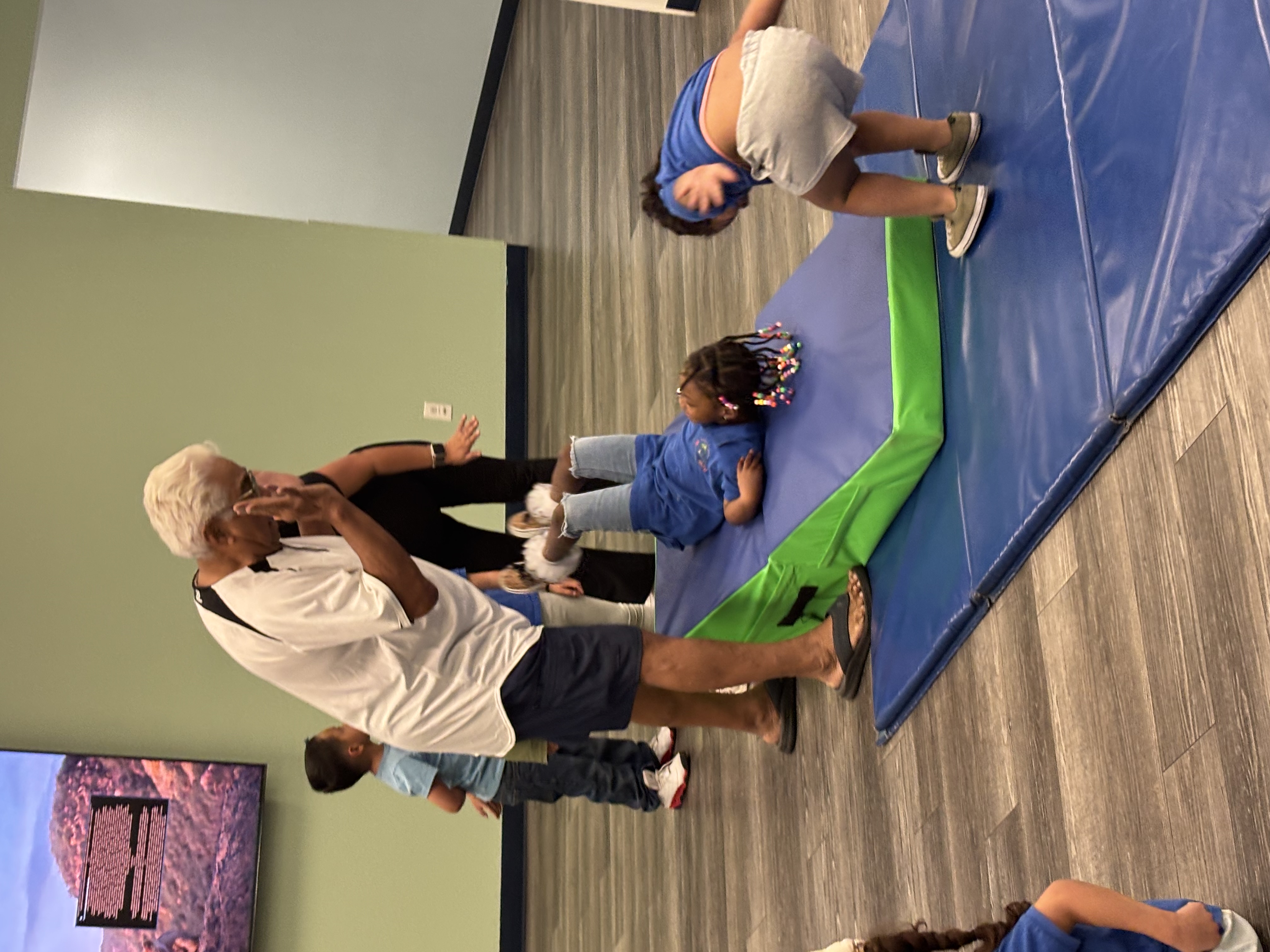 Mentor and children exercising, tumbling, and practicing balance play on indoor gym mats