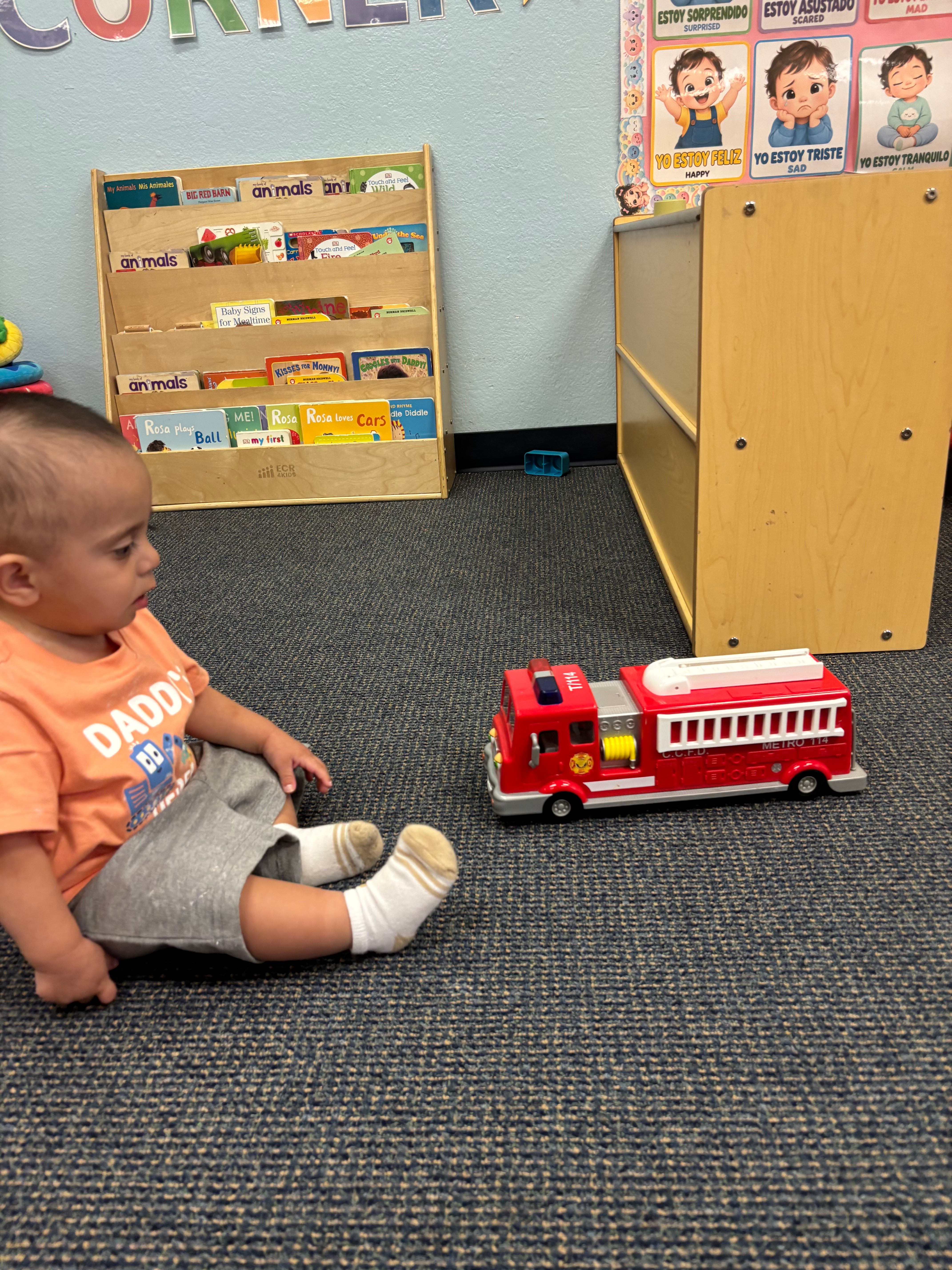 Young child in a comfortable learning corner beside bookshelves and comfort toys