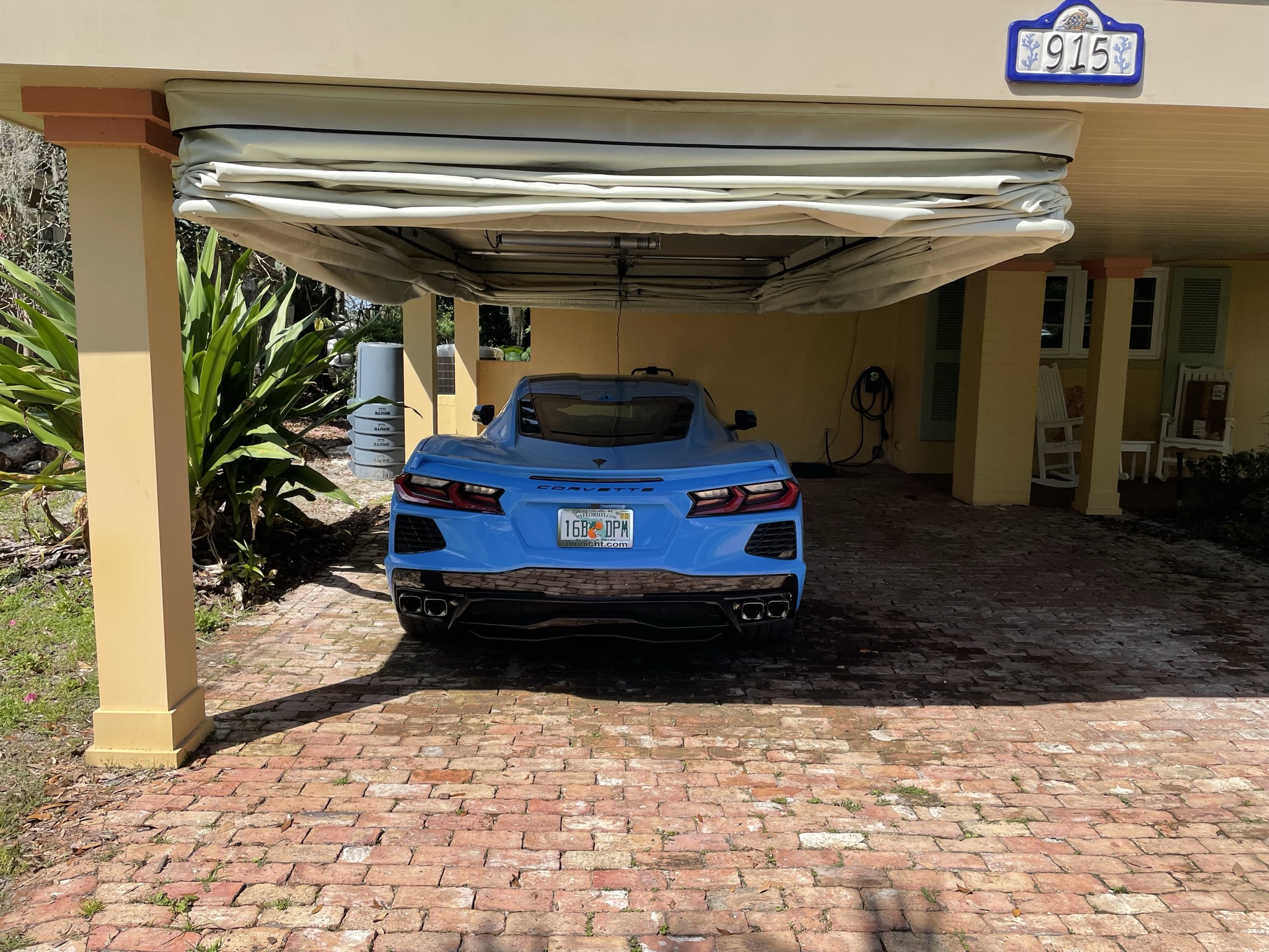 Blue Corvette parked under an open retractable Touchless Cover at a residential home