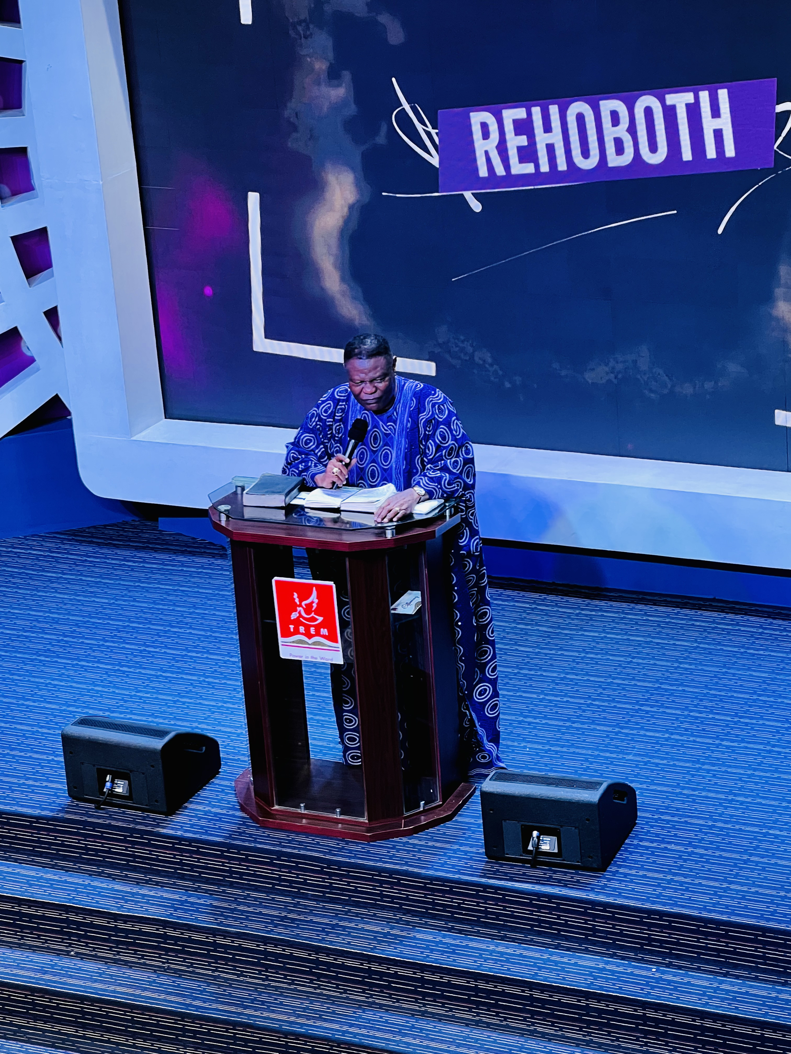 Pastor at pulpit with REHOBOTH display