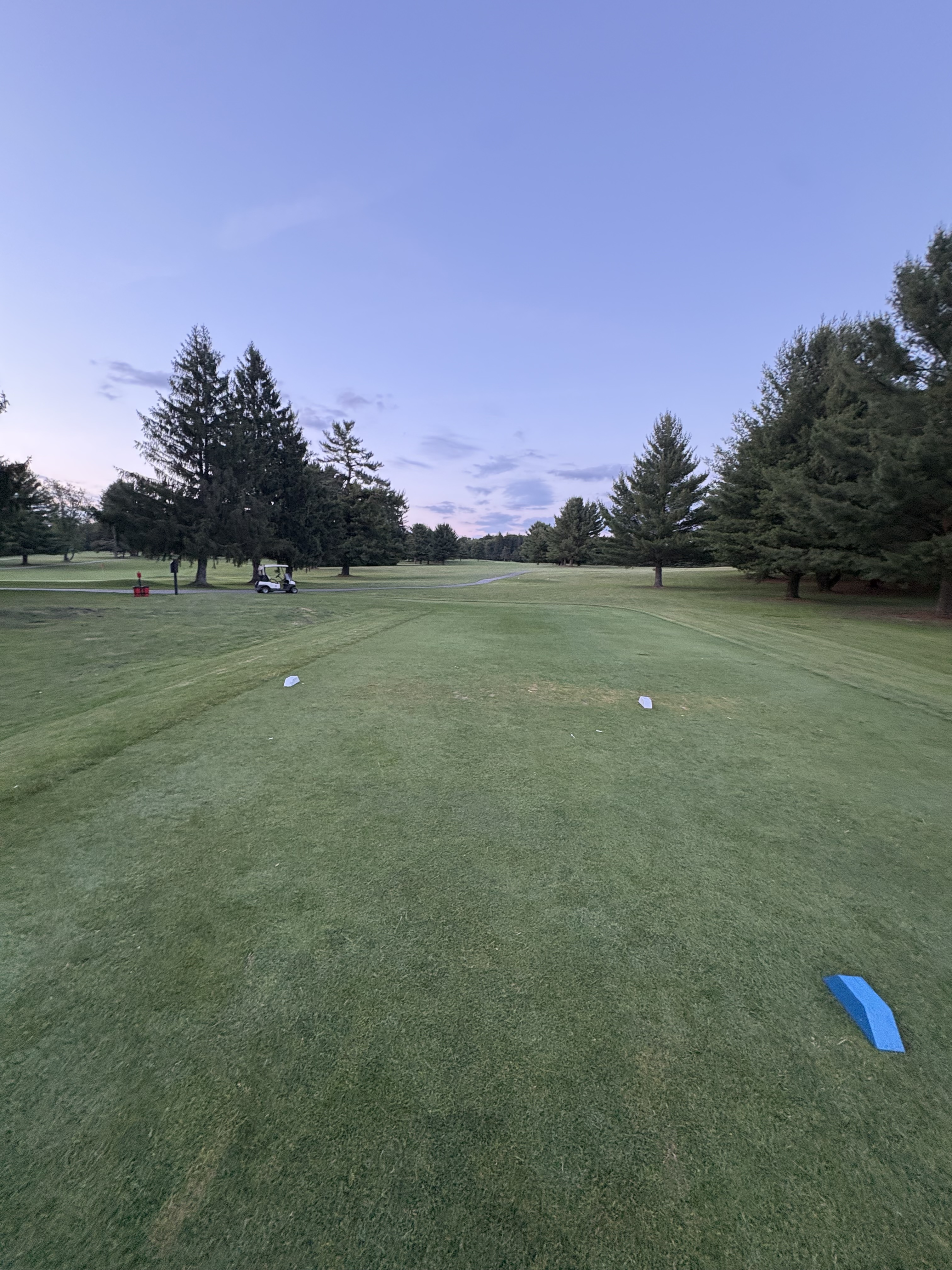 Tee box view down the fairway with a parked cart and twilight sky