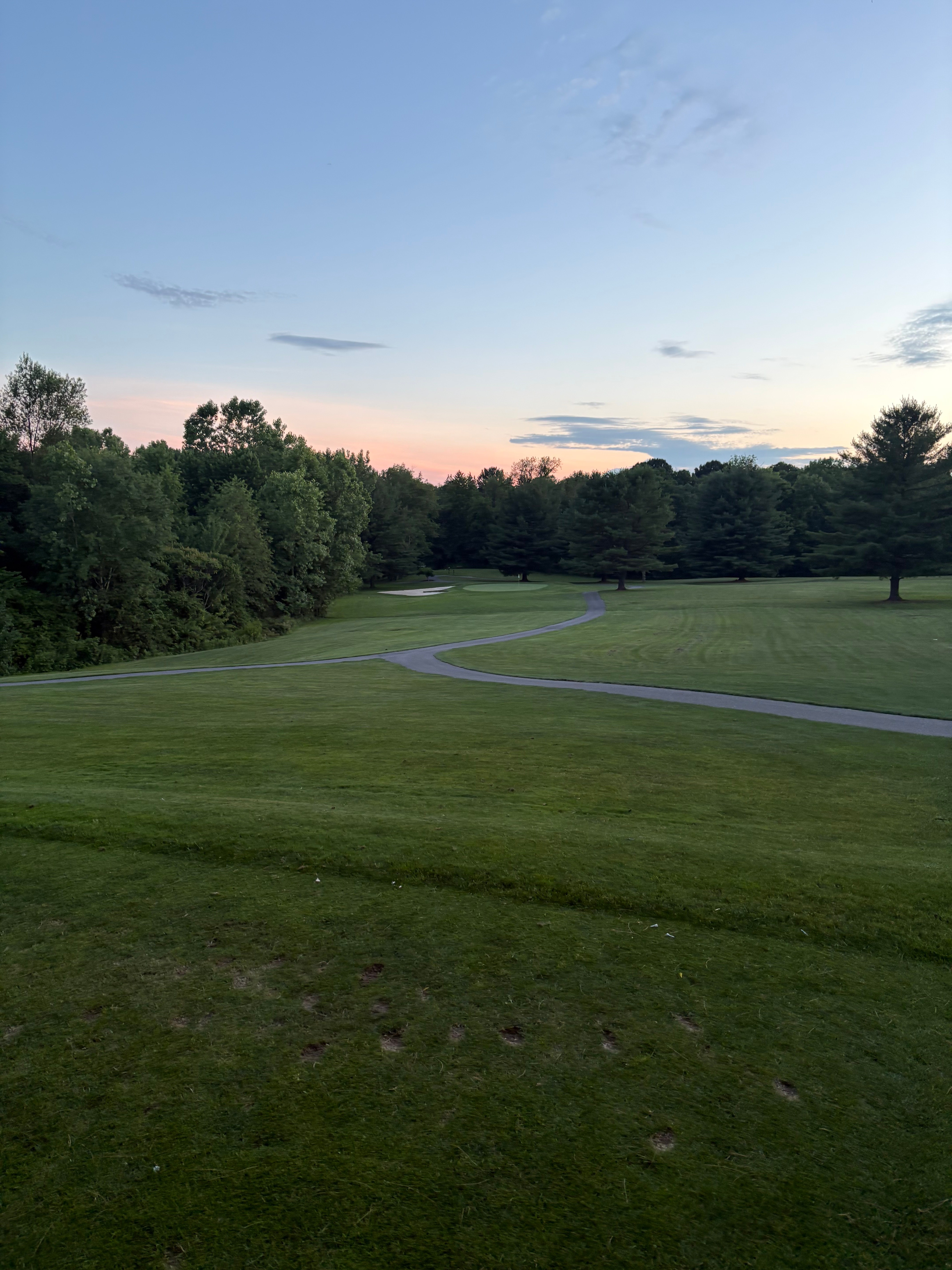 Winding cart path leading to a green with bunkers at sunset