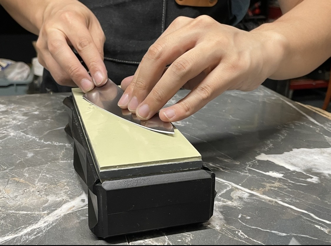 Close-up of hands angling a blade against a diamond whetstone mid-sharpening