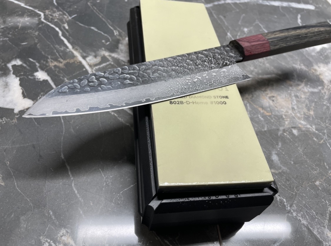 Hammered Damascus knife with purple pakkawood handle resting on a diamond sharpening stone