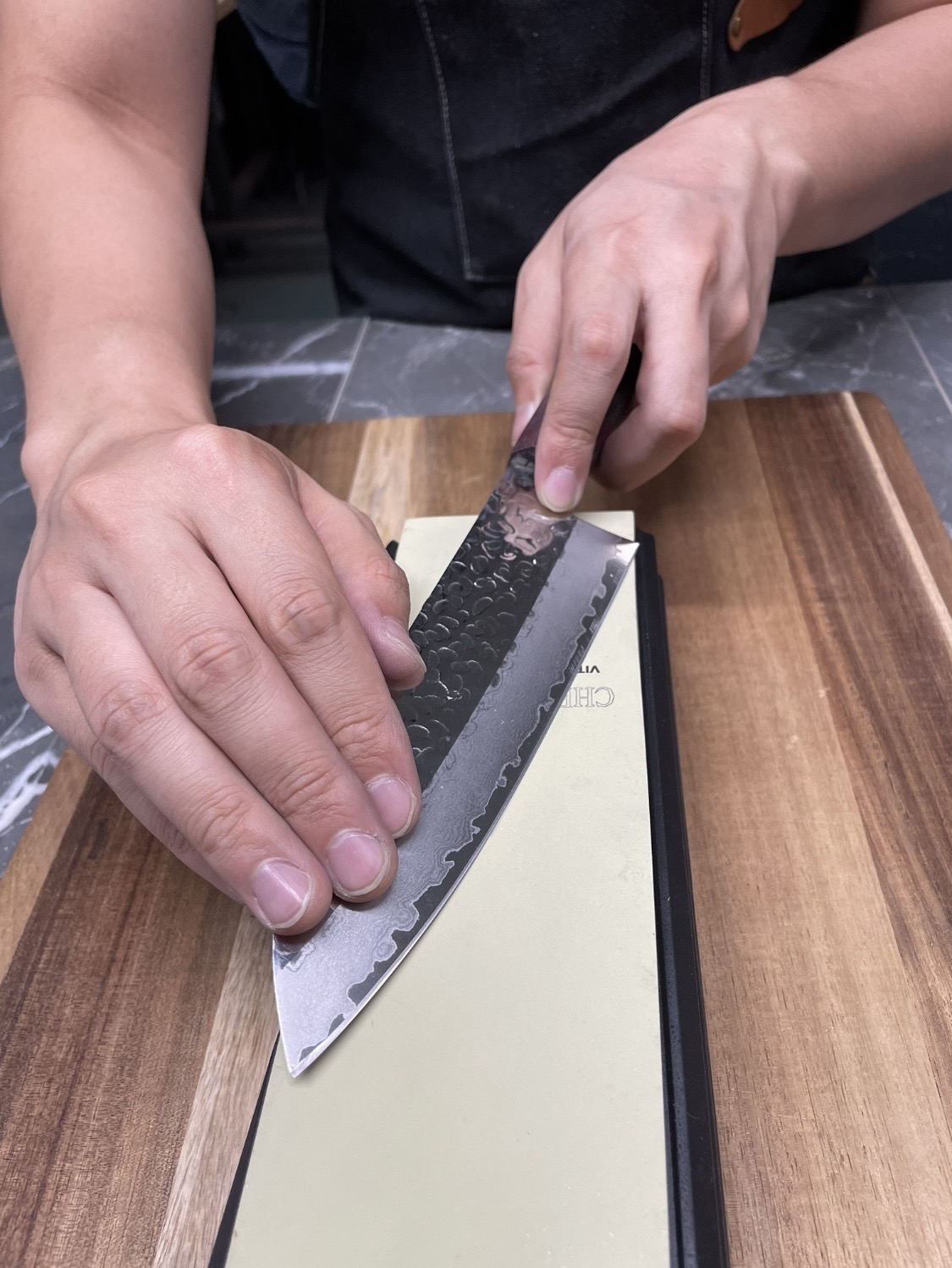 Hands guiding a hammered Damascus chef knife across a whetstone during sharpening