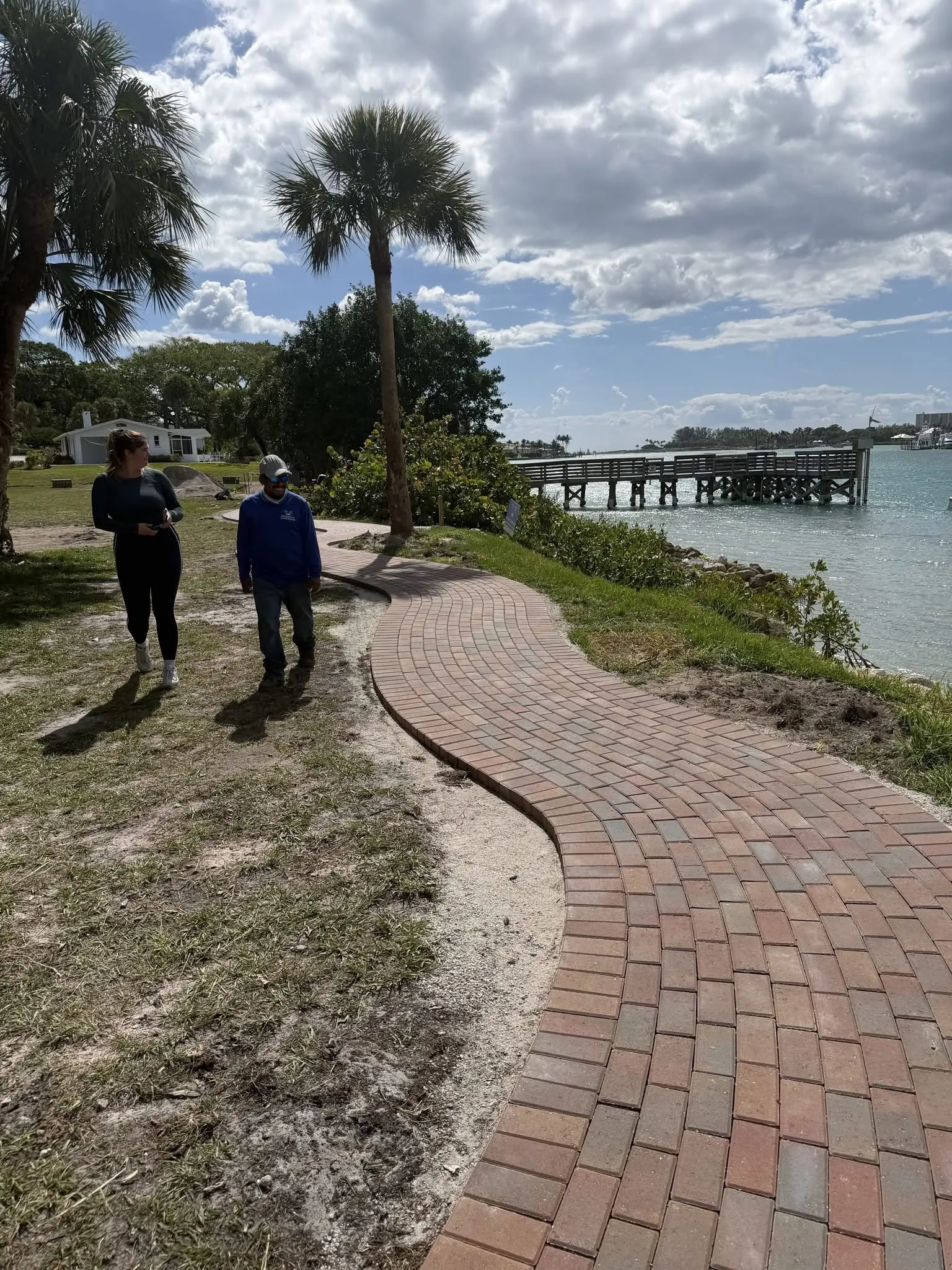 Hardscape paver walkway installation by Integrity Landscape showing a curved red-brick herringbone pathway winding along a waterfront property with a private dock and turquoise water in Jupiter, Florida
