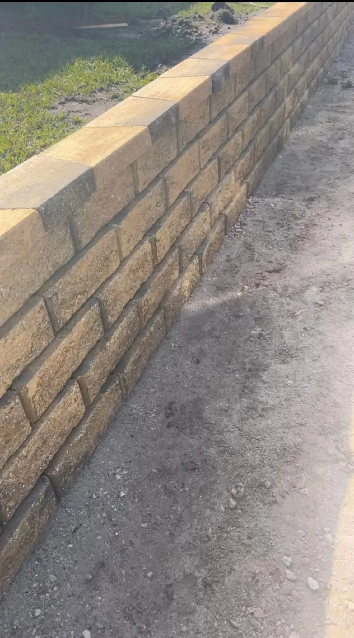 Retaining wall construction by Integrity Landscape showing a freshly completed tan and gold concrete-block retaining wall with a smooth cap course alongside a gravel pathway
