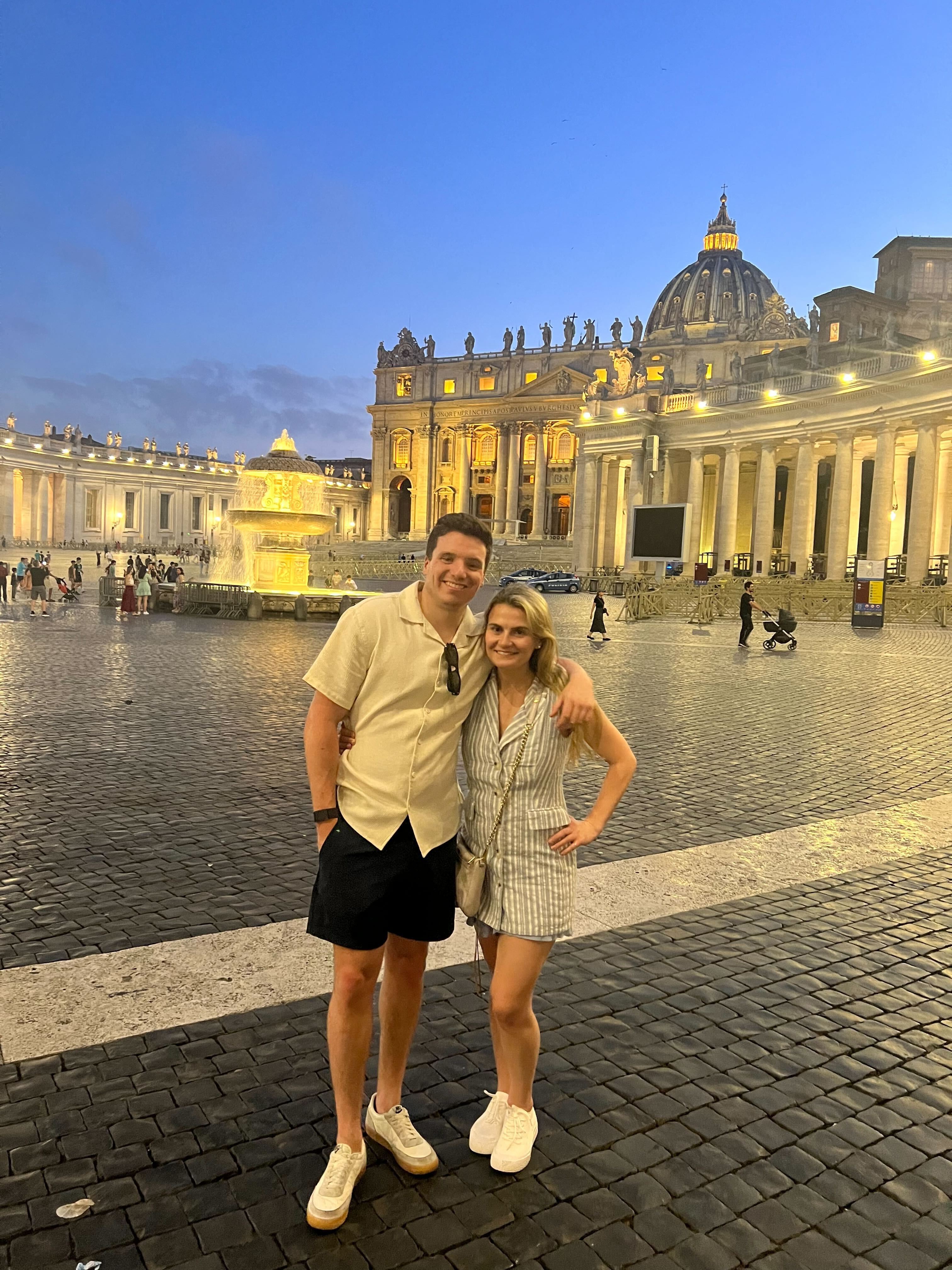 Ben and Brooke in St. Peter's Square at Vatican City during sunset, with the illuminated basilica in the background