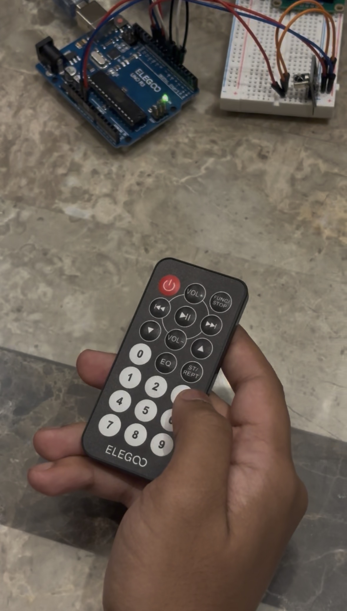 Hand holding the Elegoo infrared remote used to enter user IDs, with the Arduino circuit in the background