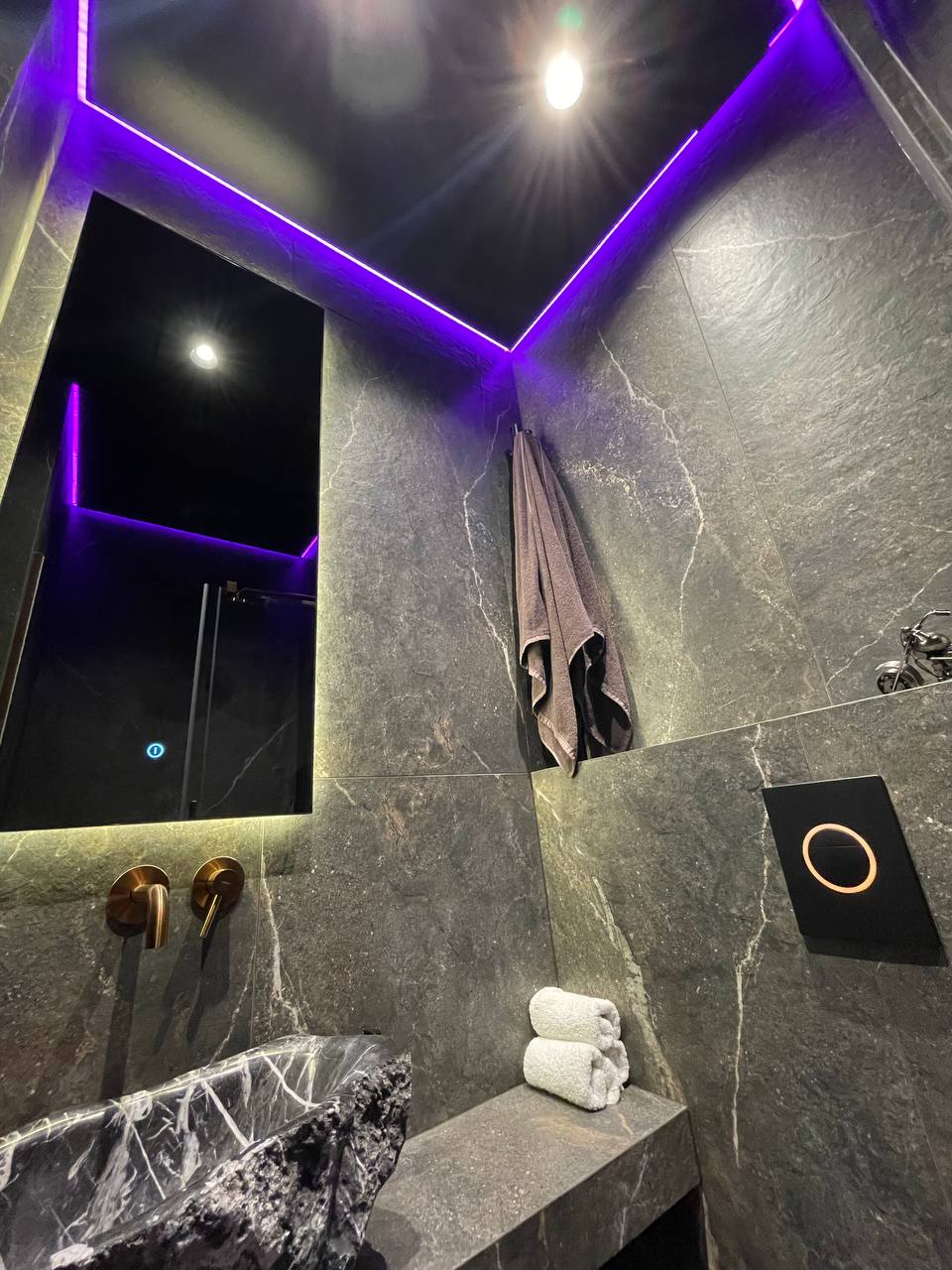 Dark marble bathroom with purple LED ceiling cove and rose-gold faucets