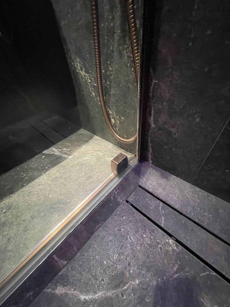 Close-up of shower enclosure base with rose-gold hardware and linear drain detail