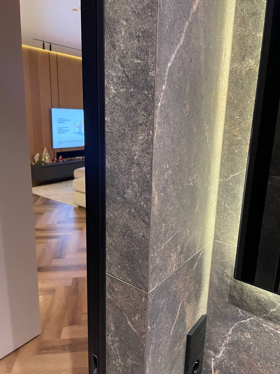 Dark marble tile column with precision mitered corners, glimpse of warm living room