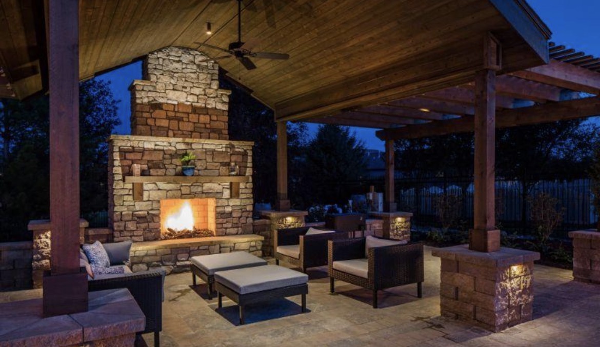 Covered outdoor living space with stone fireplace and evening ambiance