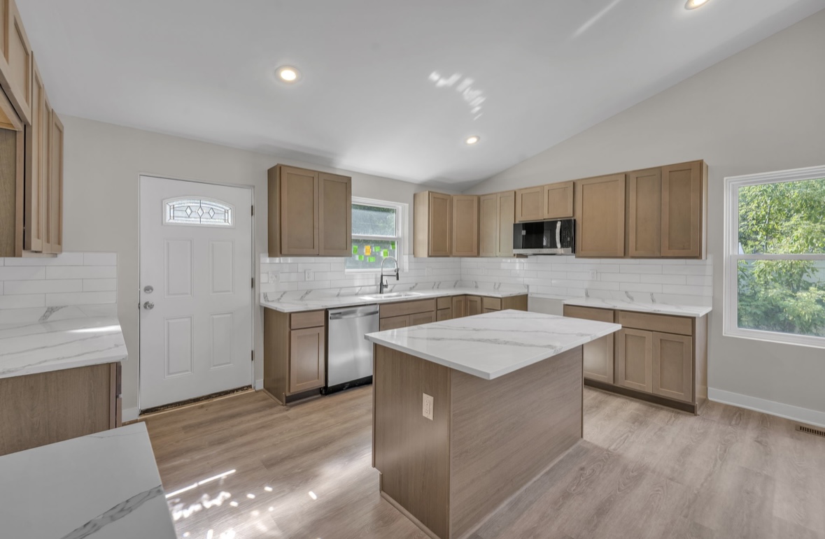 Bright kitchen with stainless dishwasher, island and decorative glass front door