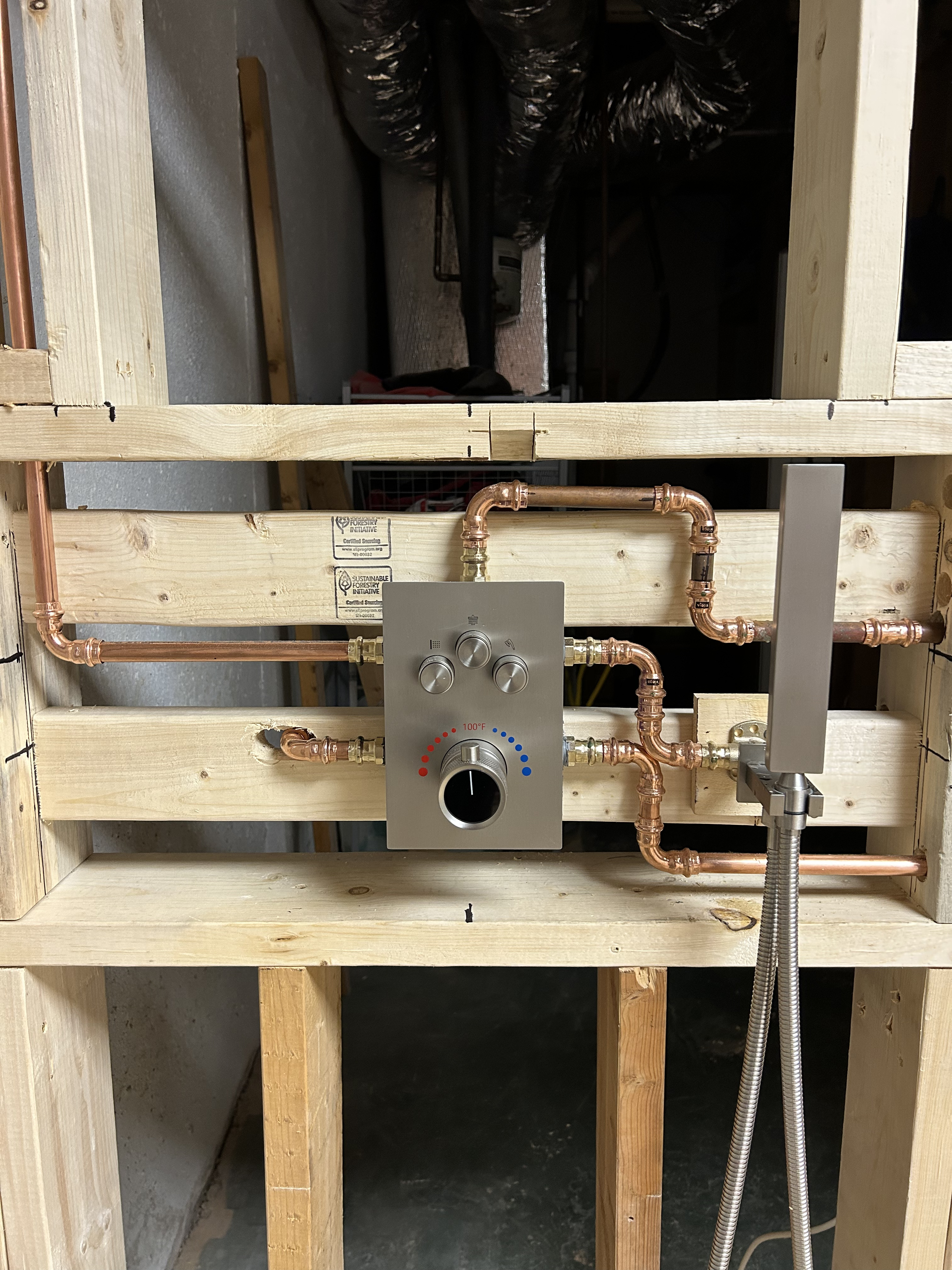 Brushed nickel thermostatic shower valve mounted in stud framing with copper supply lines and hand shower bracket
