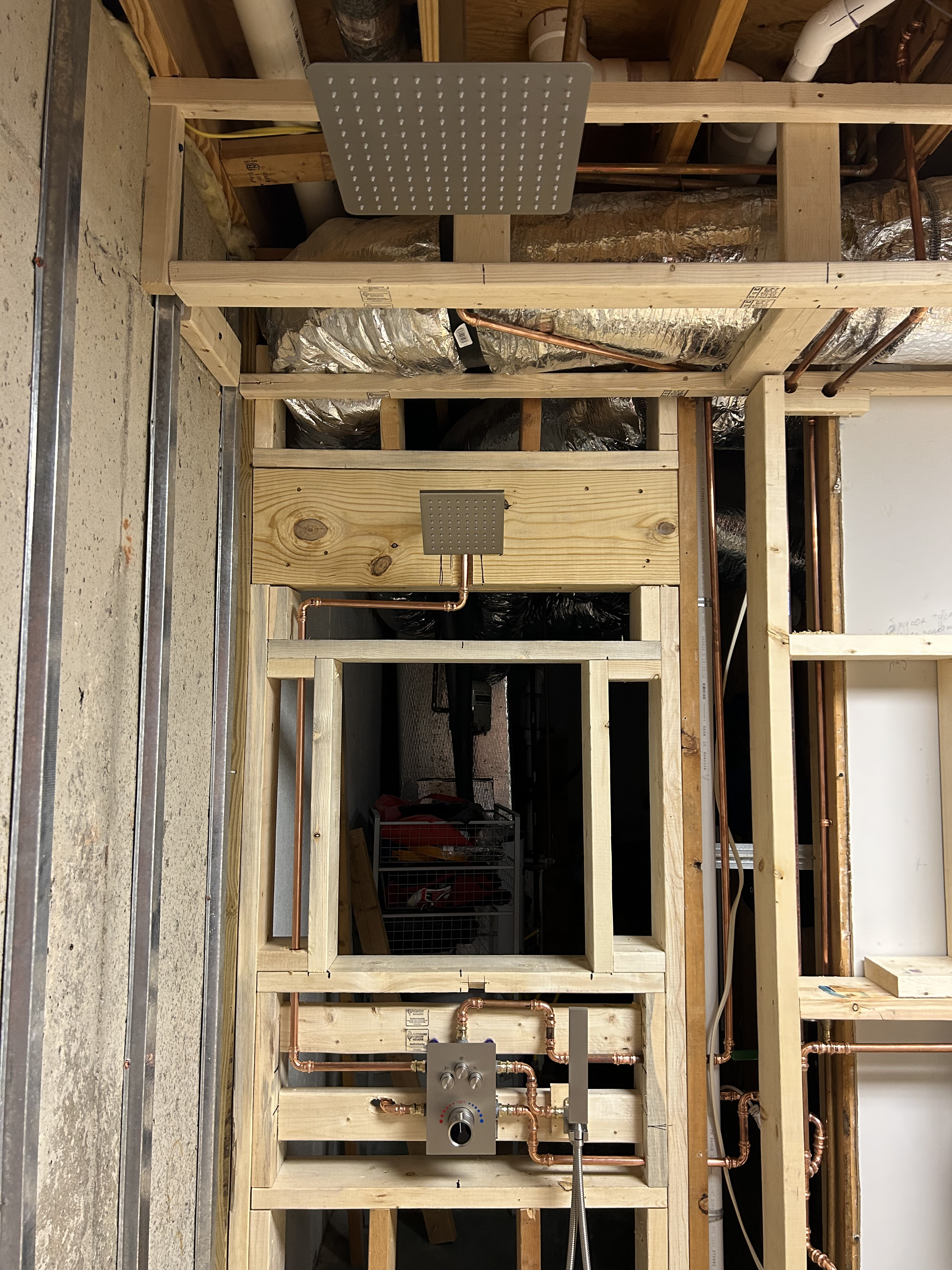 Wide shot of shower framing with ceiling-mounted square rain head, second wall-mount head, and full copper plumbing rough-in