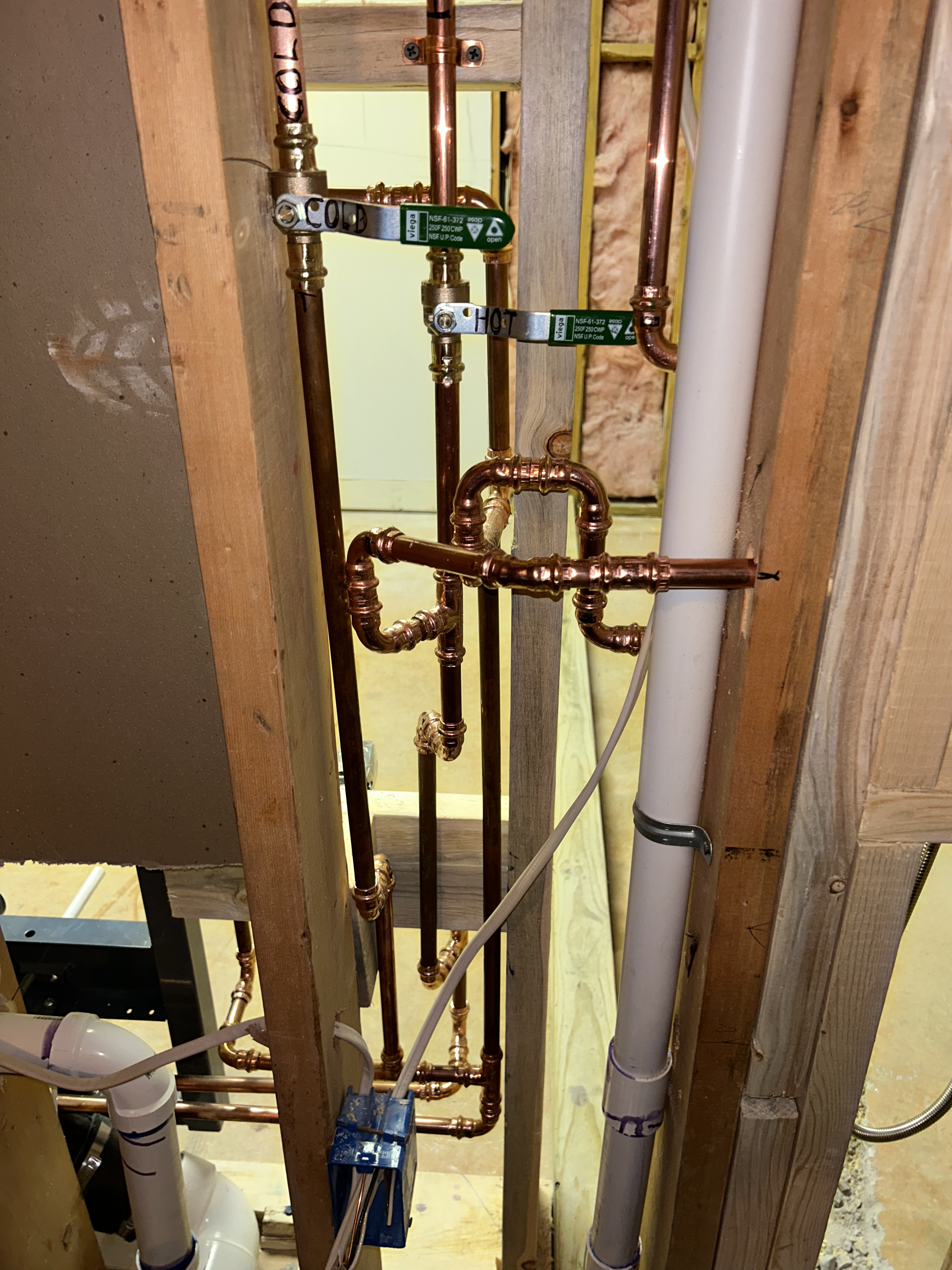 Precision copper pipe rough-in with labeled hot and cold supply lines and clean solder joints inside open wall framing